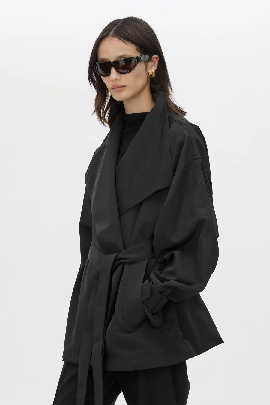 Woman wearing a black coat and sunglasses on a white background