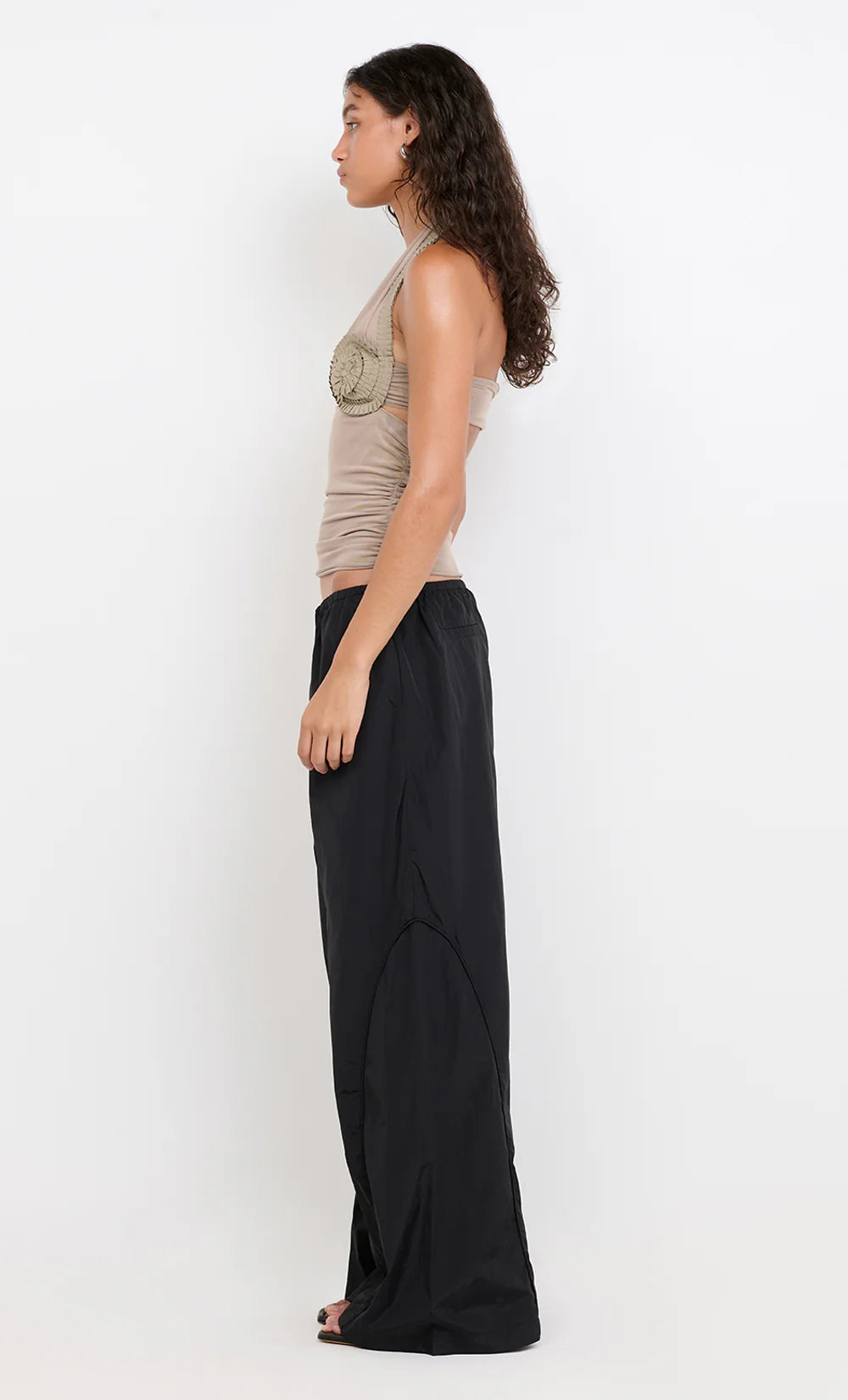 Woman wearing a beige sleeveless top and black wide-leg pants on a white background