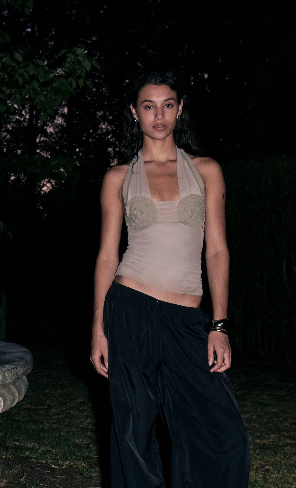 Woman wearing a beige top and dark skirt standing outdoors at night.