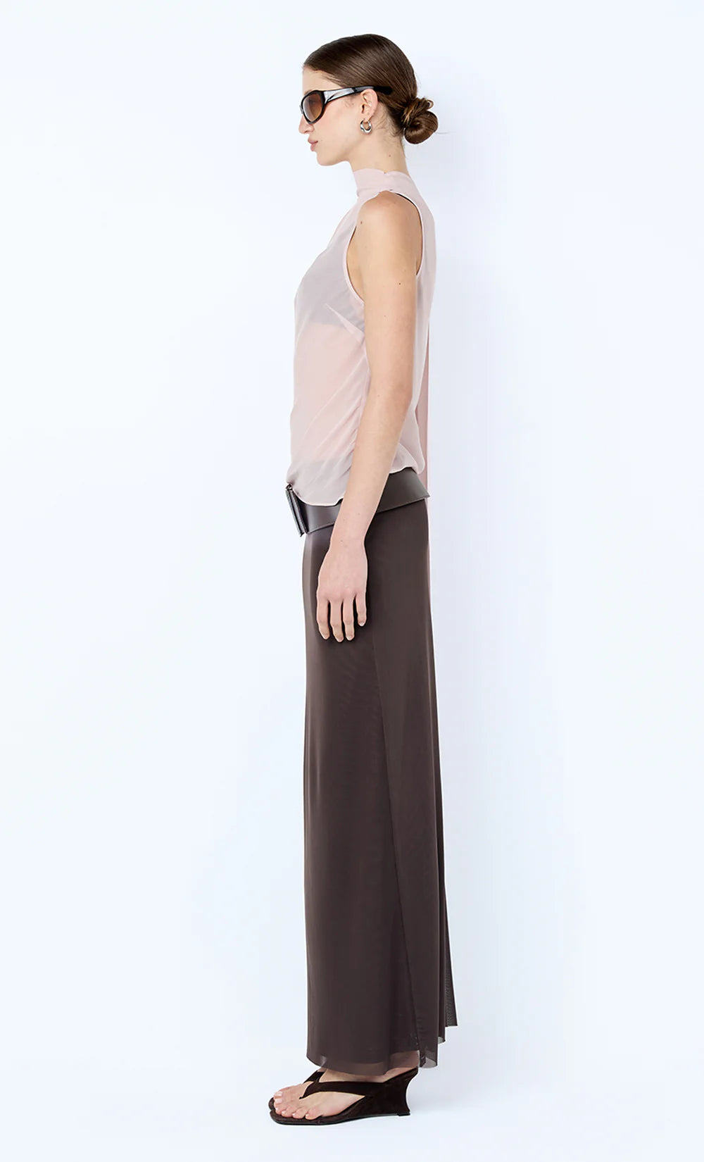 Woman wearing a sleeveless top and long brown skirt on a white background