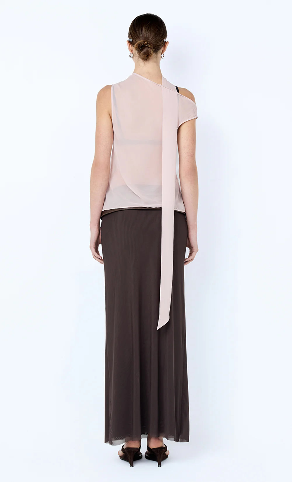 Woman wearing a light pink sleeveless top with a long brown skirt on a white background