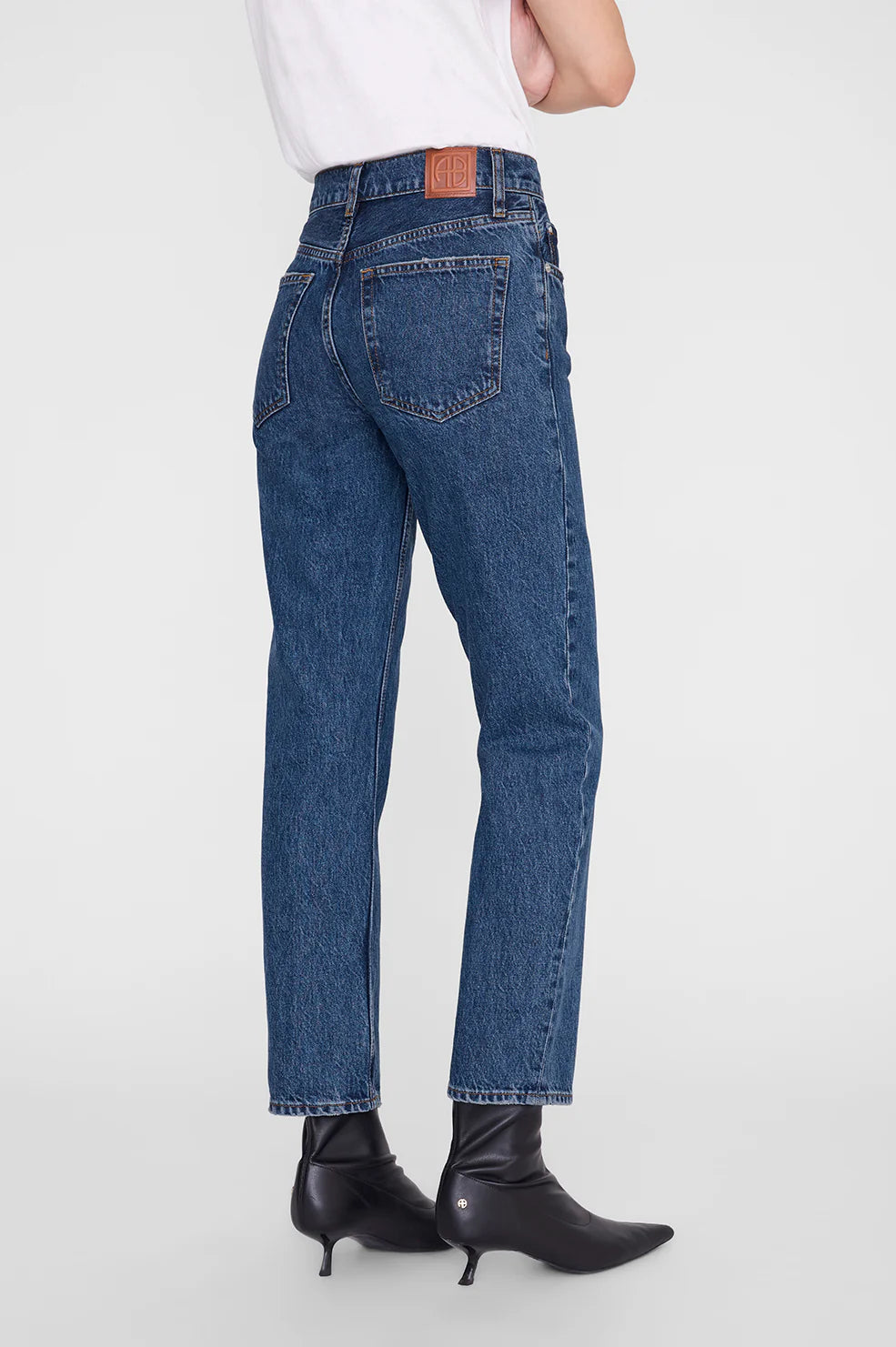Person wearing blue jeans and black boots on a white background