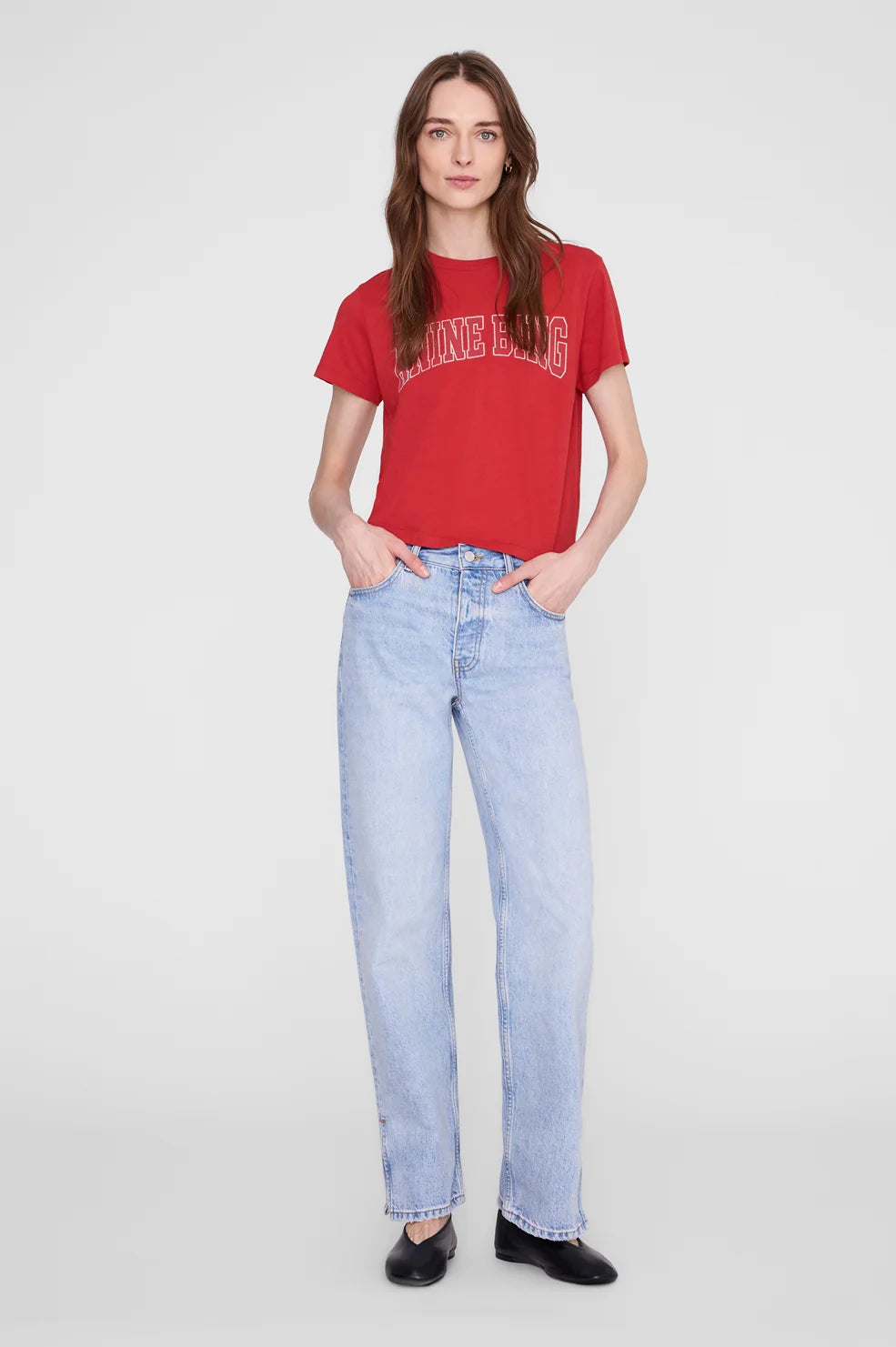 A woman modeling a red graphic t-shirt and light-wash blue jeans against a plain light gray studio background.