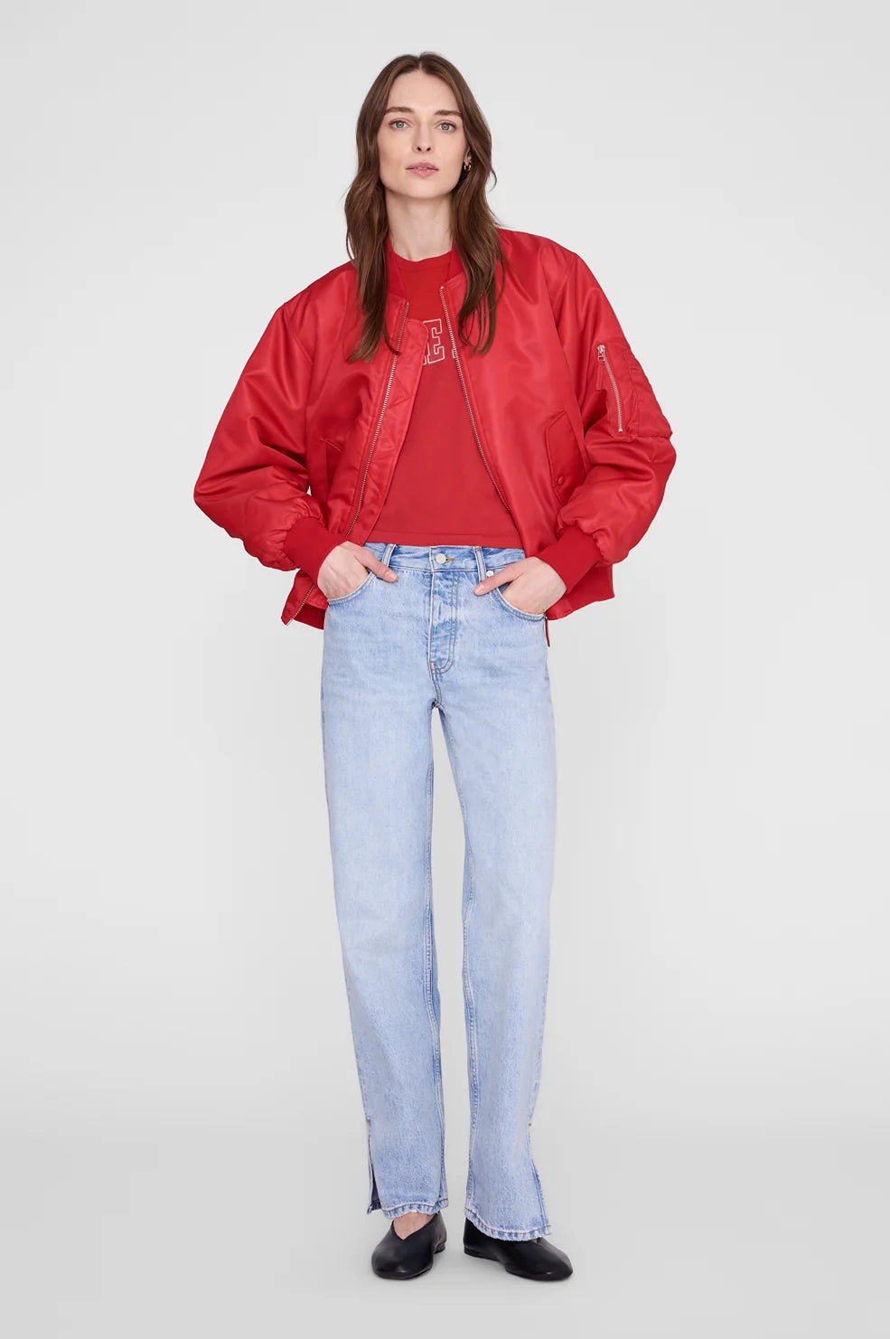 A woman modeling a red satin bomber jacket over a matching red top, paired with light-wash blue jeans and black shoes, against a plain light gray studio background.