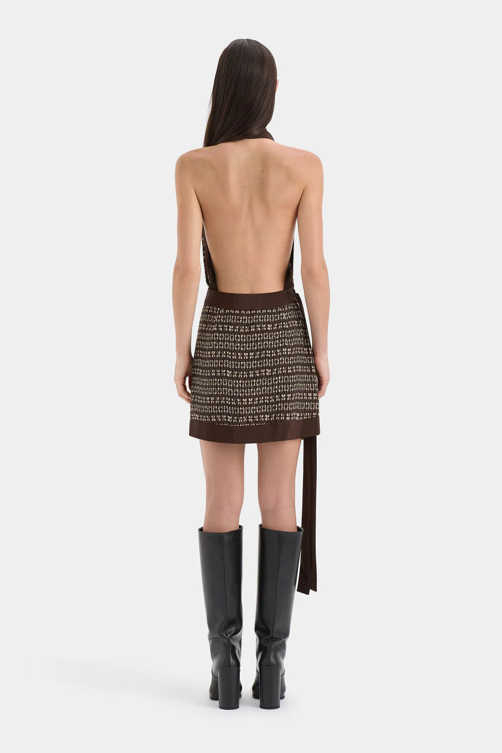 Woman wearing a backless dress with a pattern and black knee-high boots on a white background