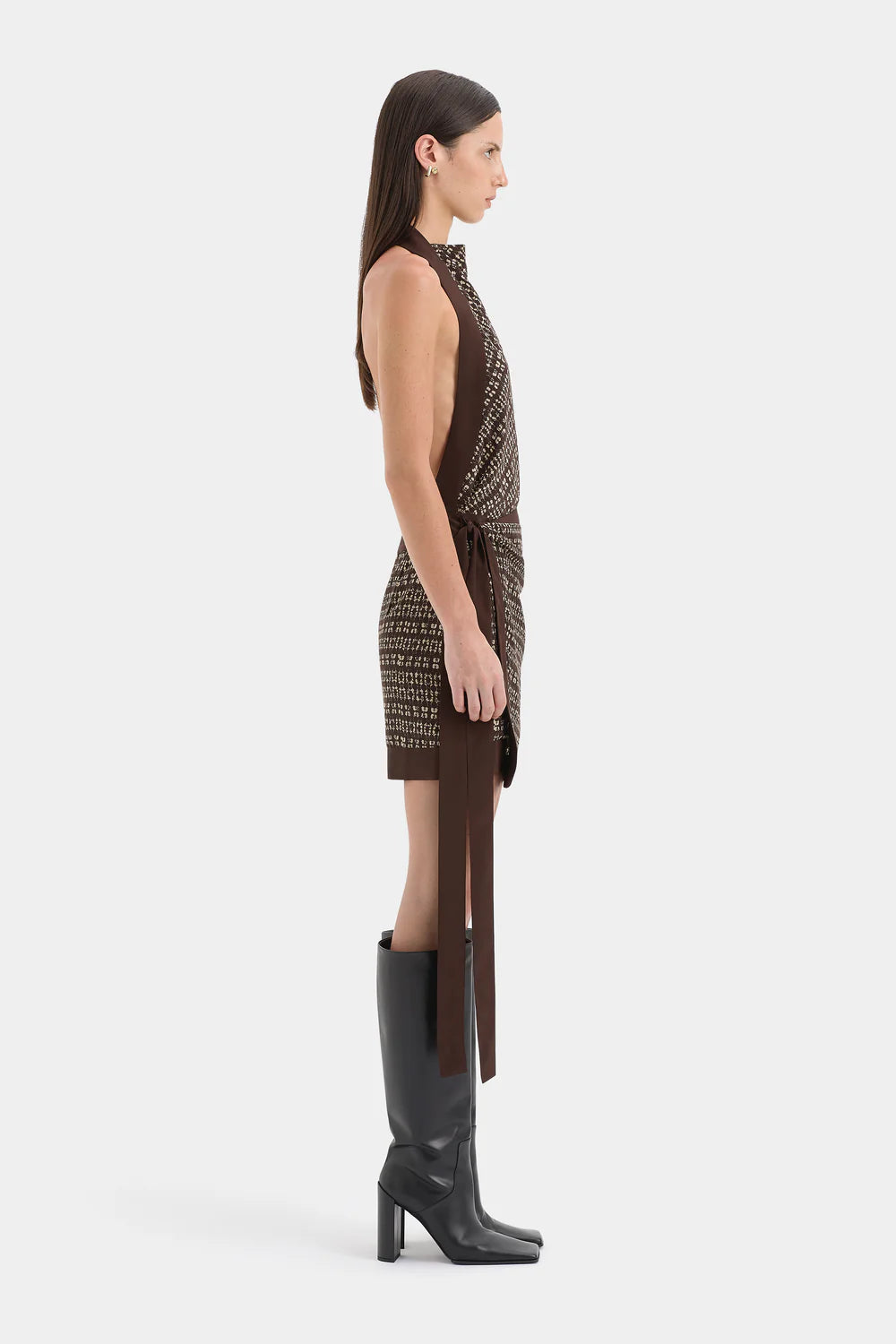 Woman wearing a patterned dress with a slit and black high-heeled boots on a white background