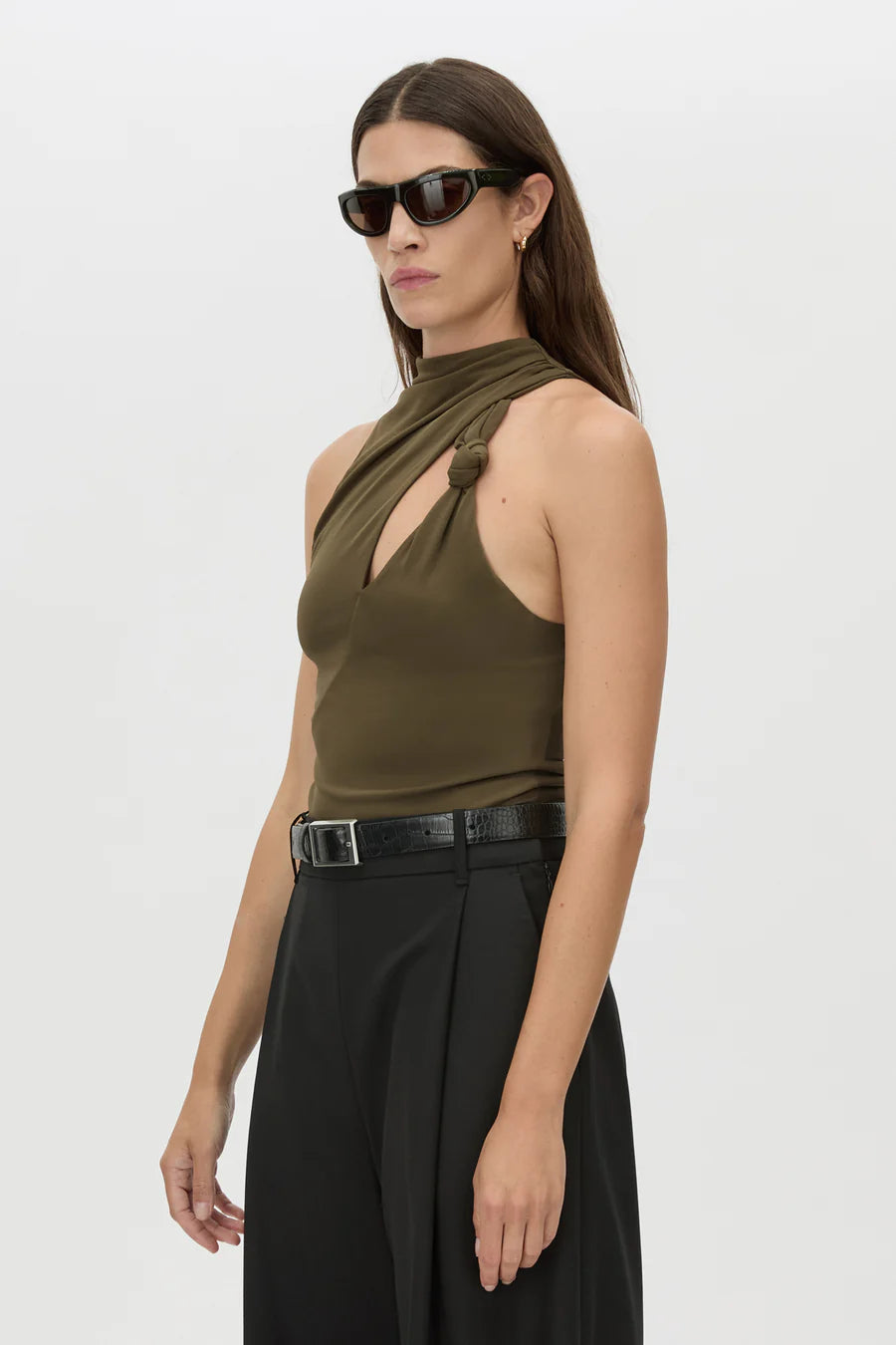 Woman wearing an olive green halter top and black pants on a white background