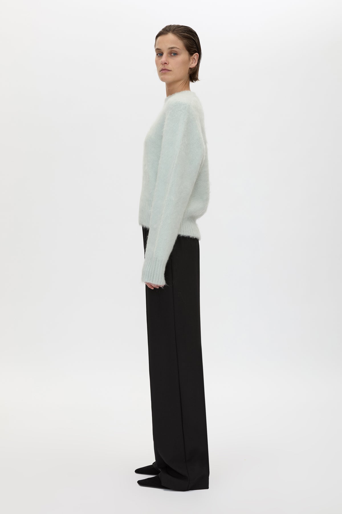 Person wearing a light green sweater and black pants on a white background
