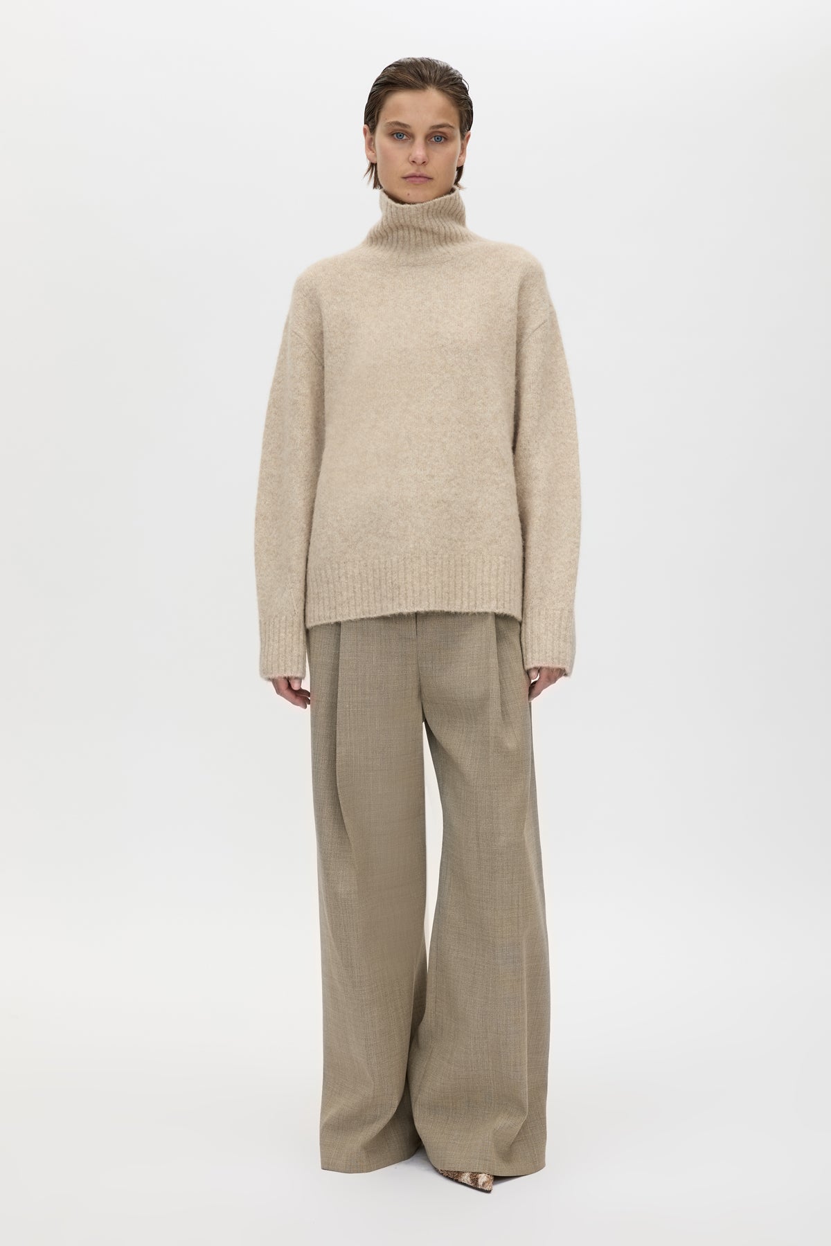 Person wearing a beige turtleneck sweater and wide-leg pants on a white background
