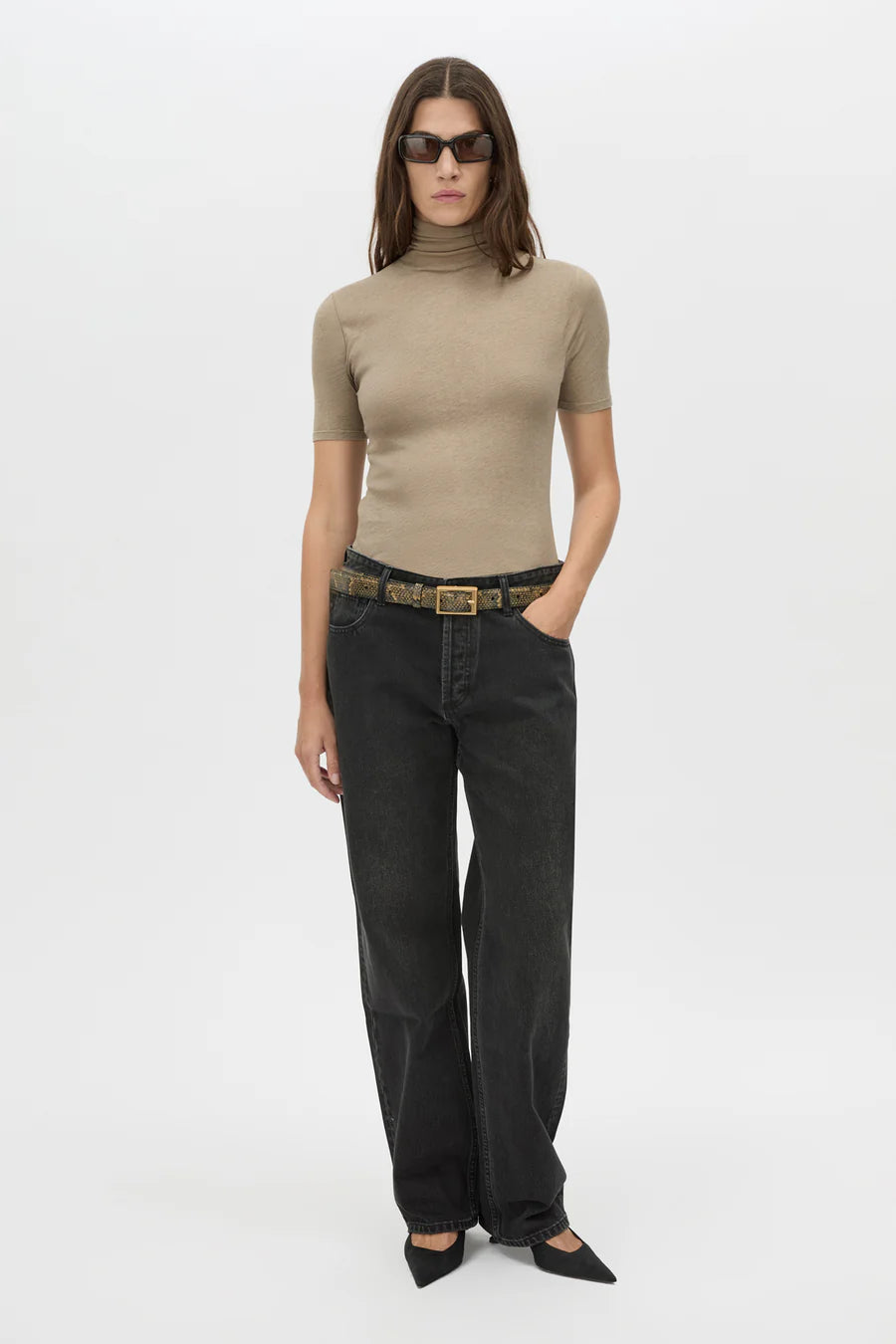 Woman wearing a beige turtleneck and black jeans on a white background