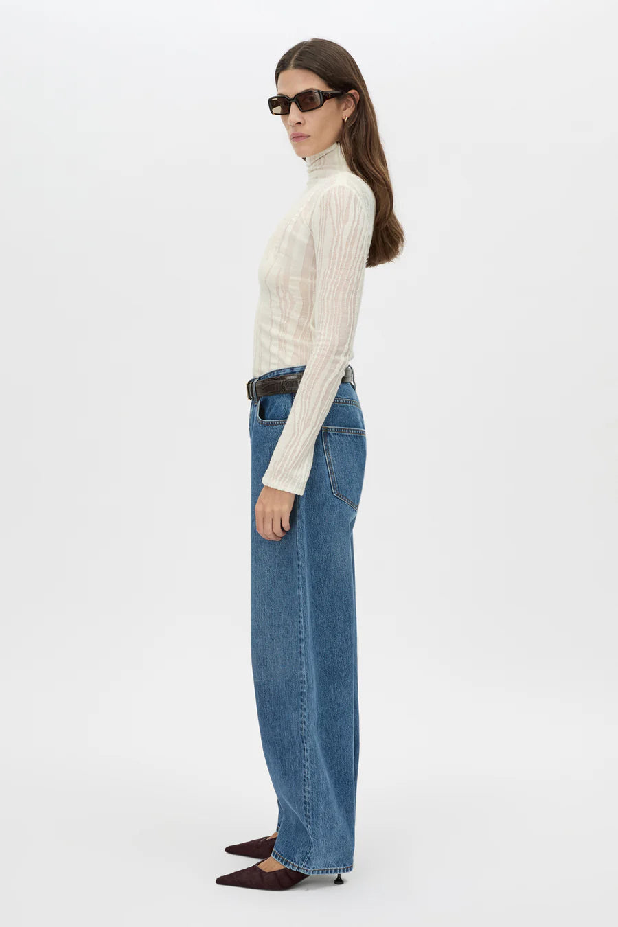 Woman wearing a cream turtleneck and blue jeans on a white background
