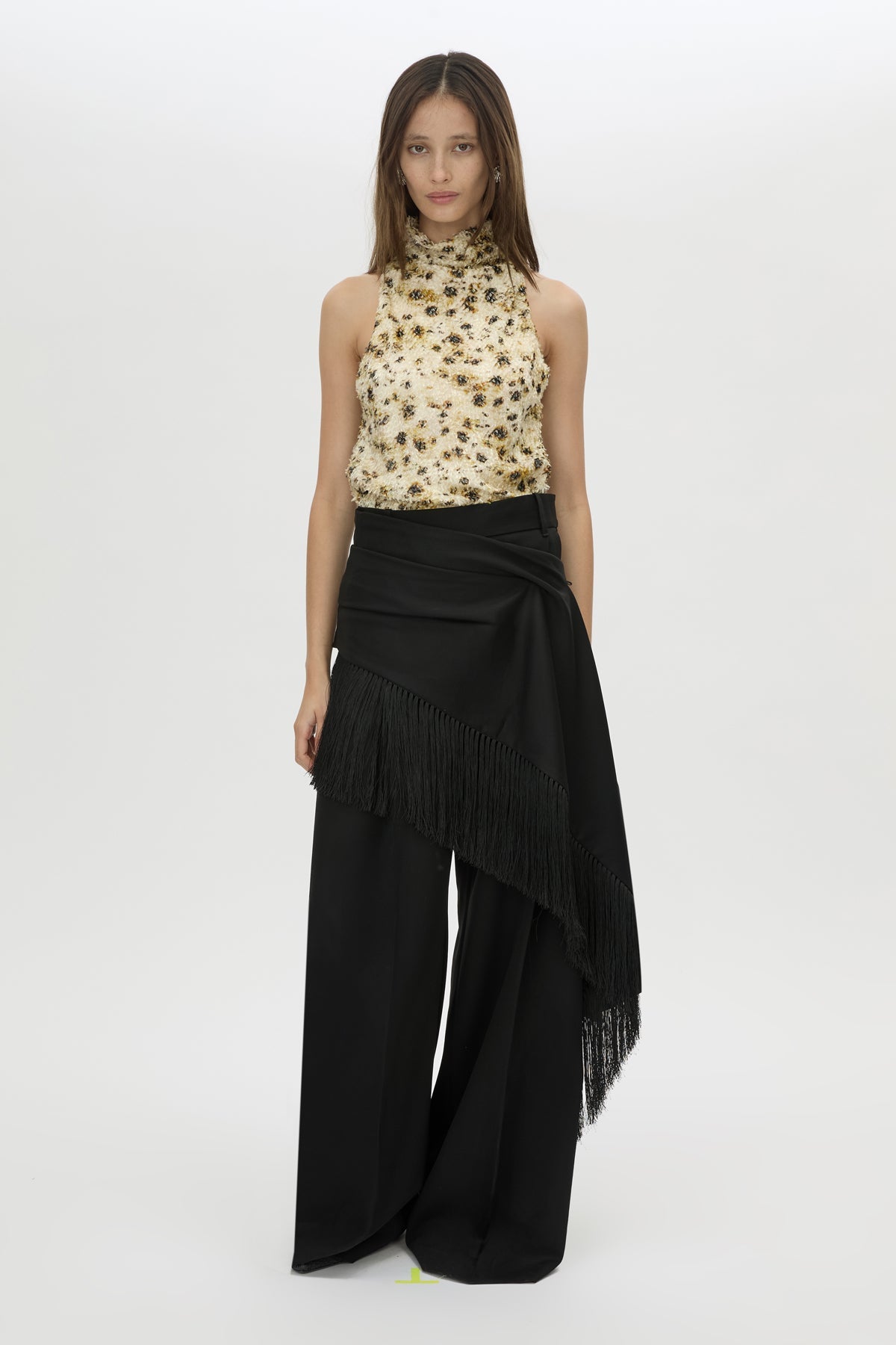 Woman wearing a floral top and black fringed pants on a white background
