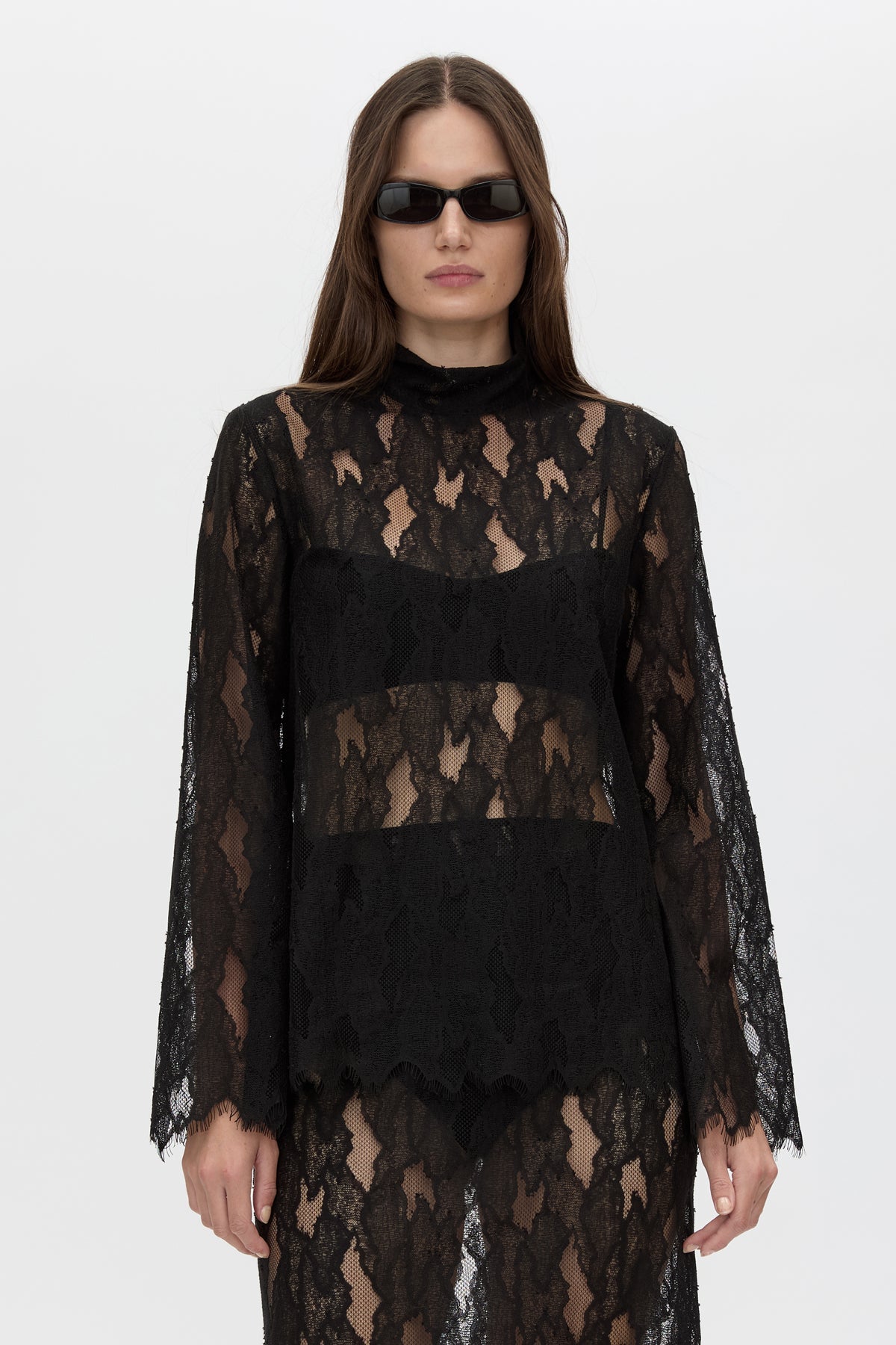Woman wearing a black lace dress with sheer sleeves on a white background