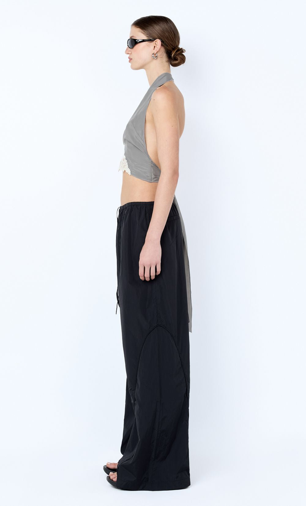 Woman wearing a gray halter top and black wide-leg pants on a white background
