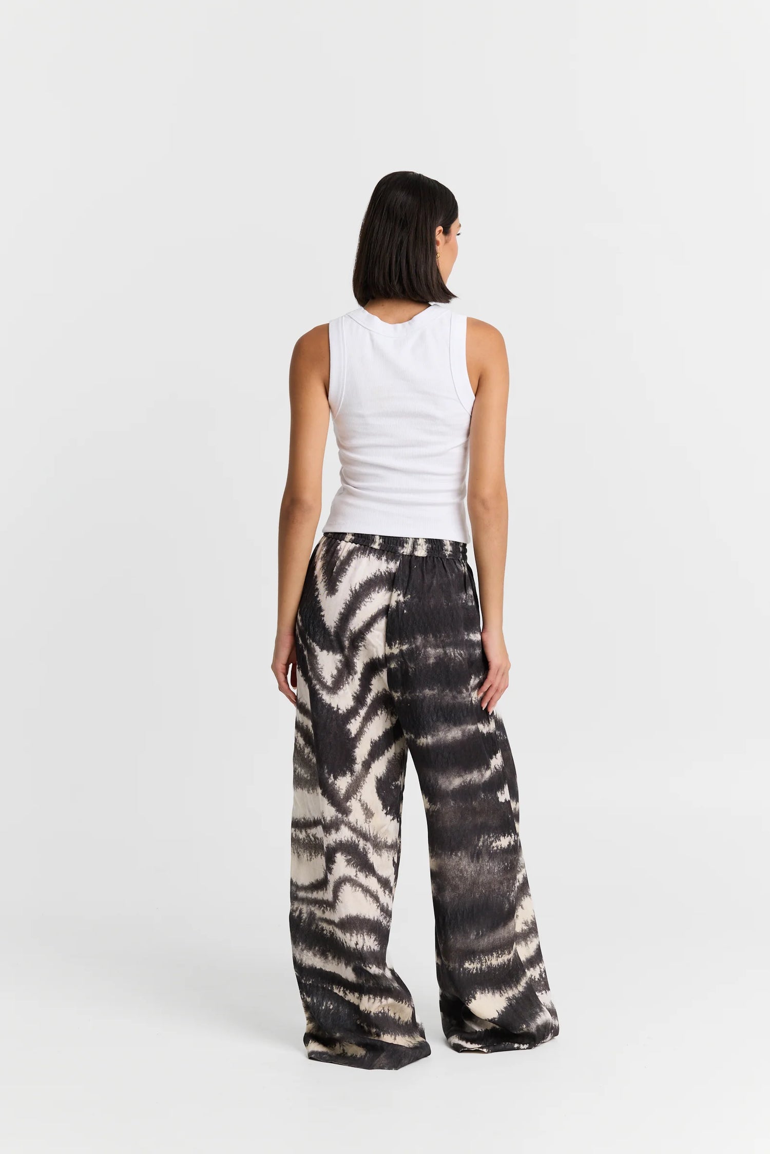 Person wearing a white sleeveless top and tie-dye pants on a white background