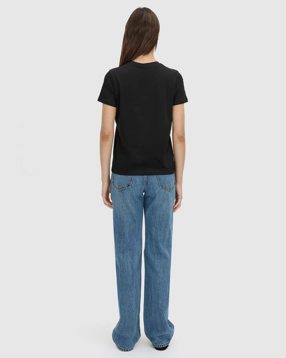 A woman is shown from the back wearing a black short-sleeve t-shirt and wide-leg blue jeans against a light gray studio background.