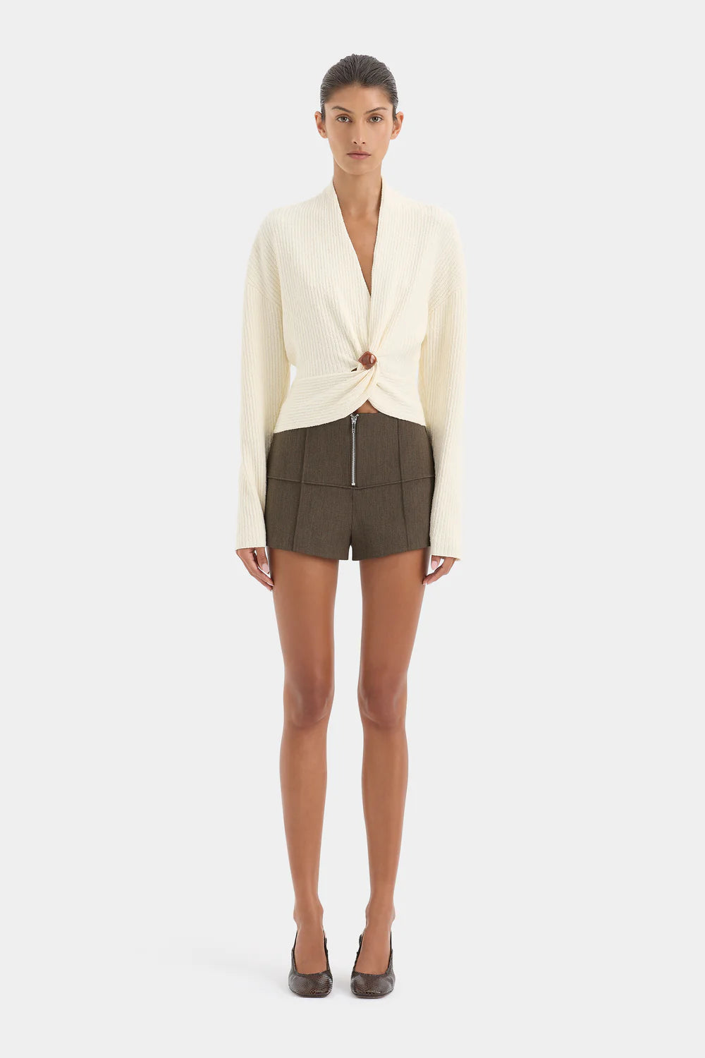 Woman wearing a cream blazer and green shorts on a white background