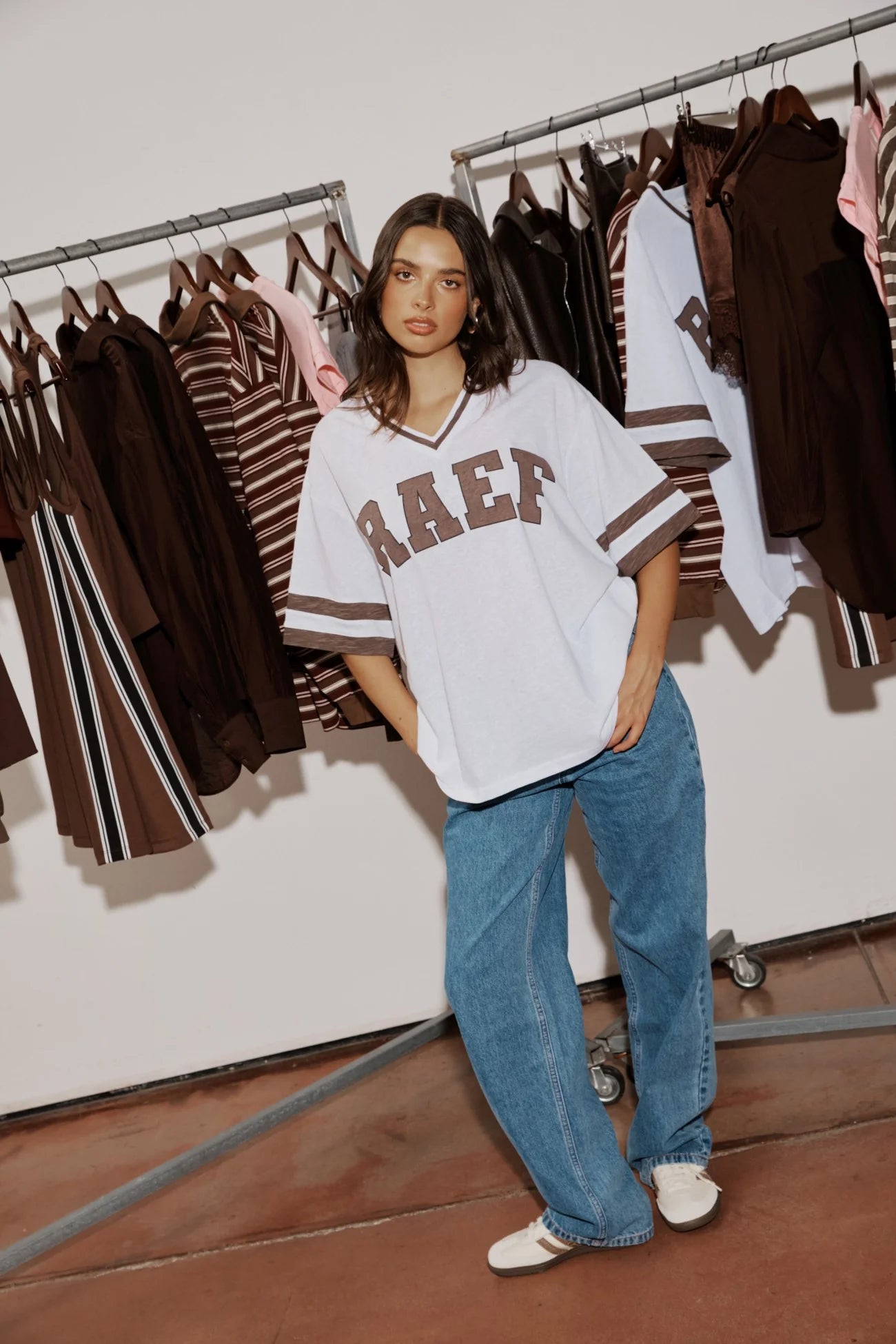 Woman standing in a cool girl white oversized tee with brown graphics and cool baggy jeans