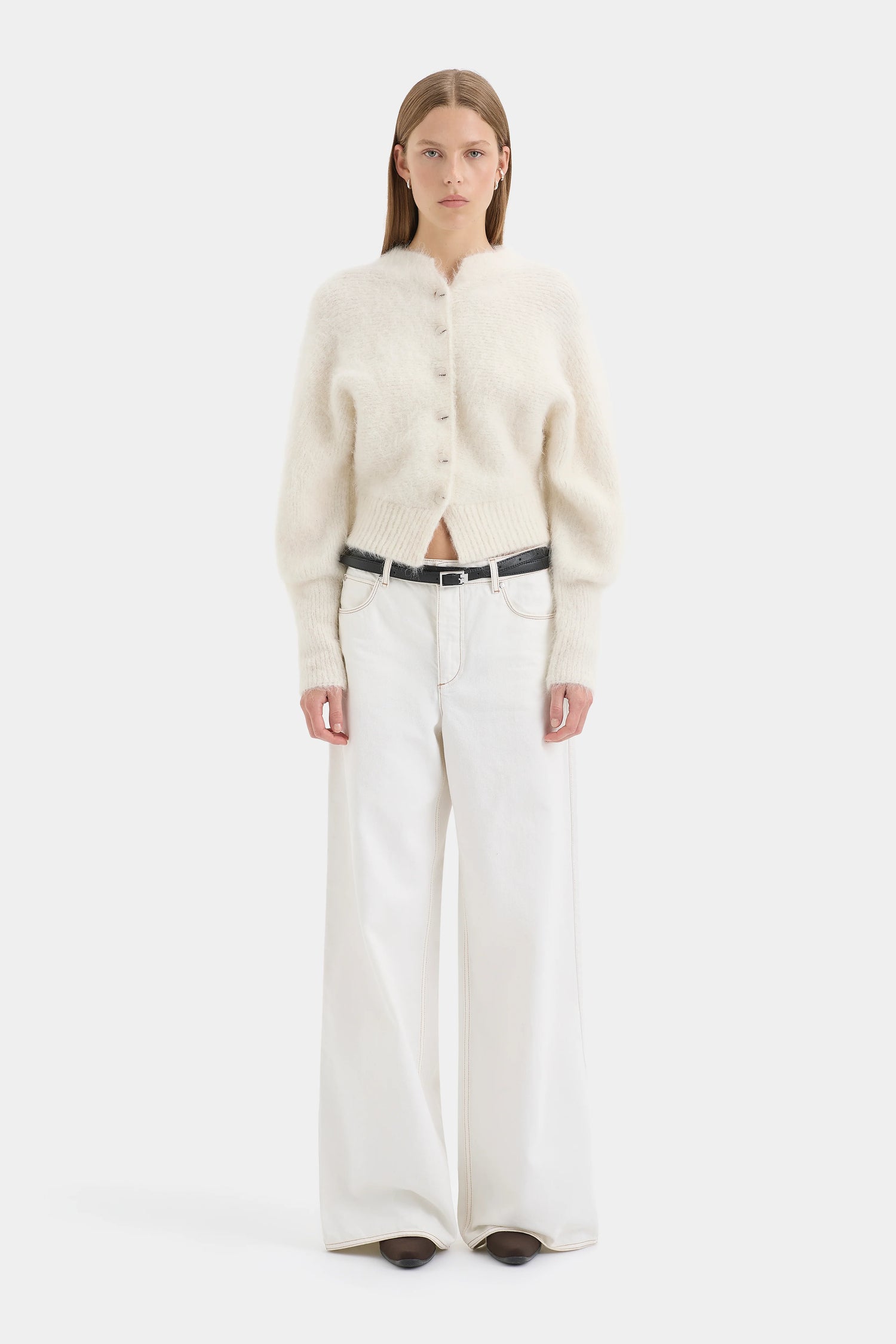 Woman wearing a cream cardigan and white pants on a white background