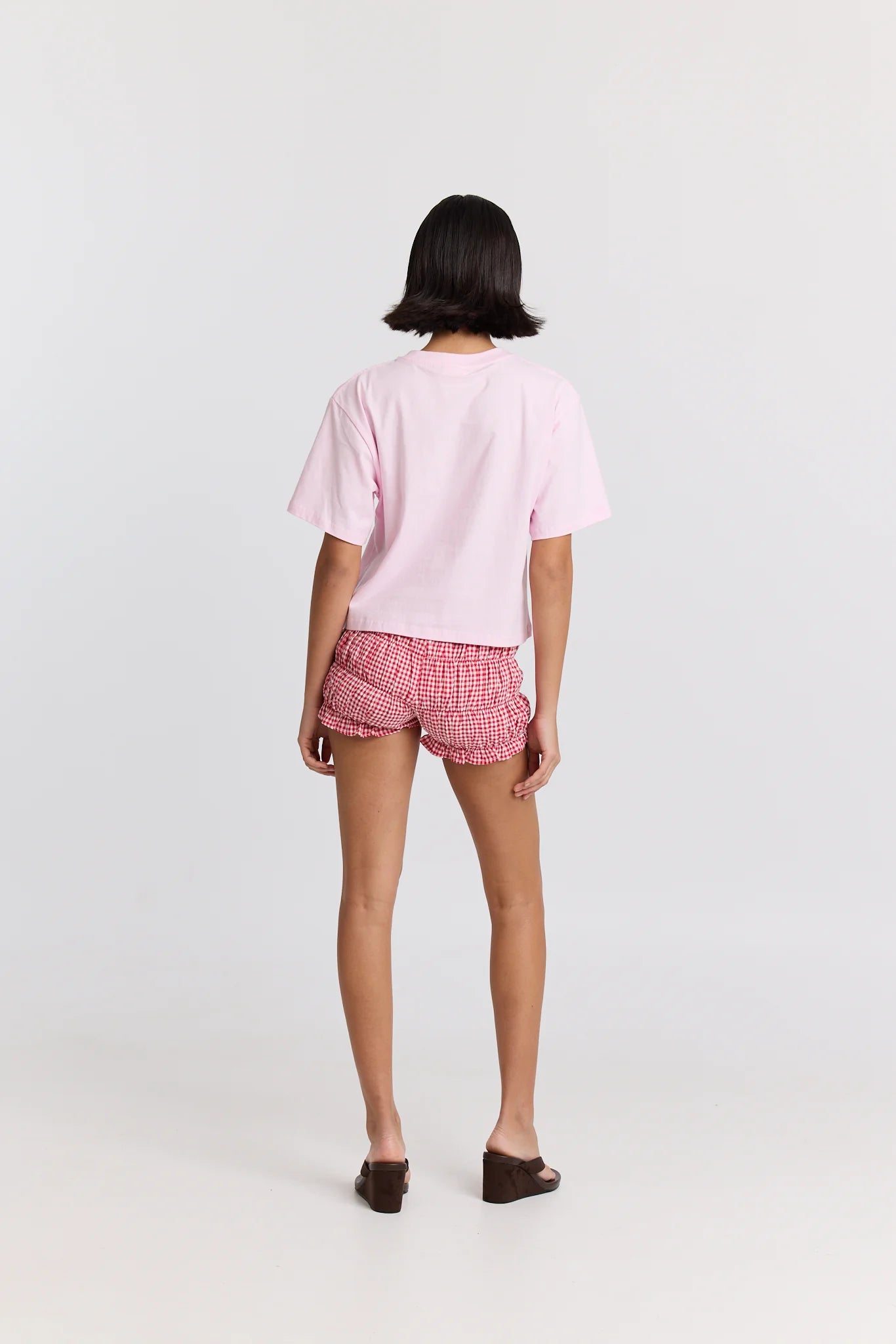Person wearing a pink t-shirt and checkered shorts on a white background