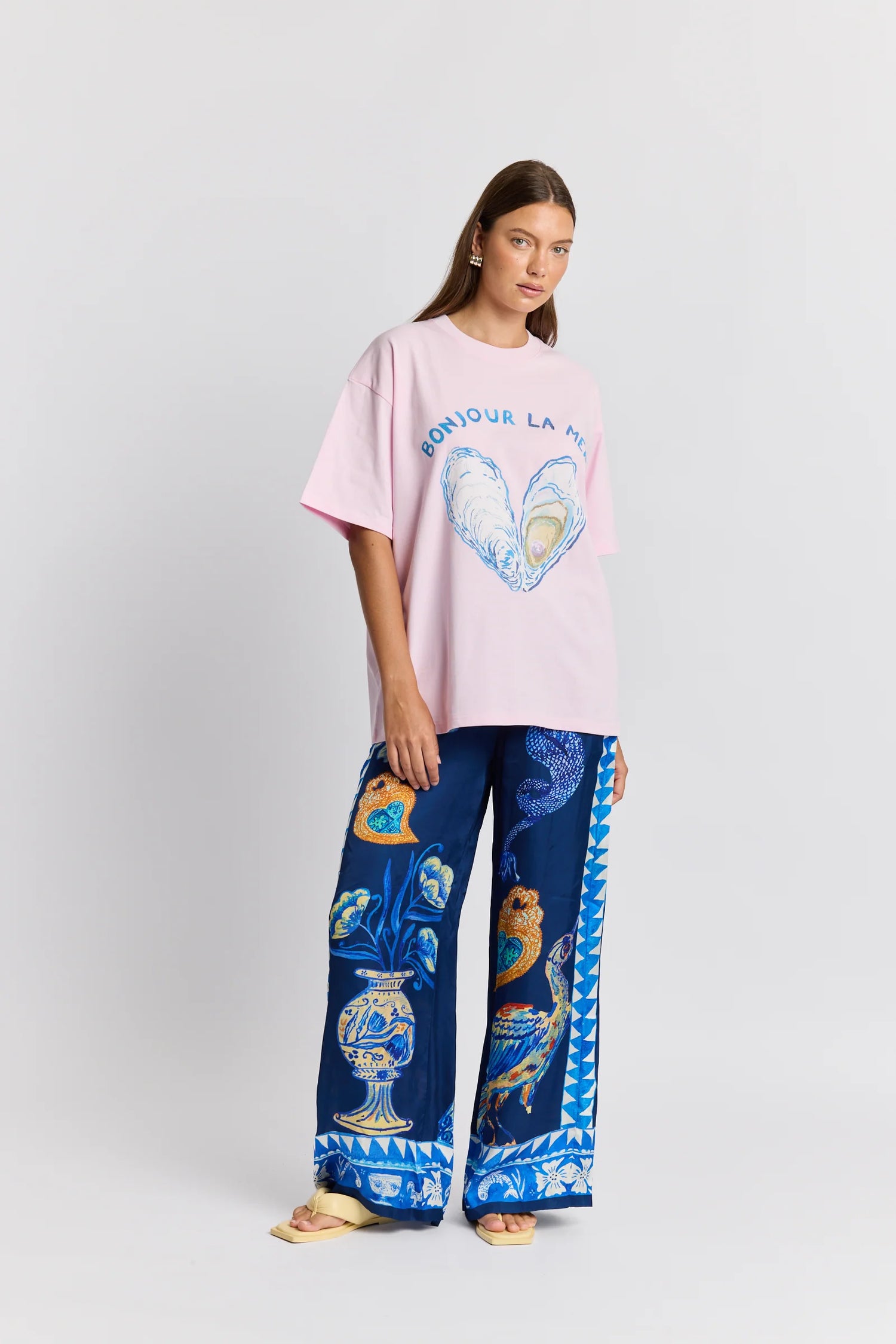 Woman wearing a pink oversized t-shirt with a graphic design and blue patterned pants on a white background