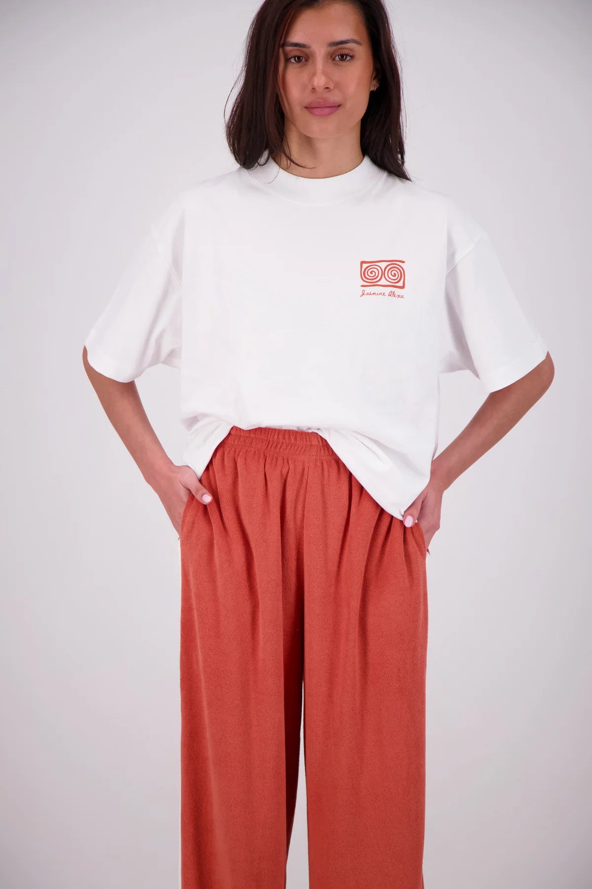 Person wearing a white oversized shirt with a small red logo and red pants on a plain background