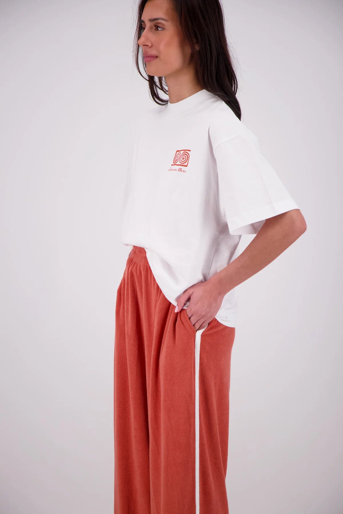 Woman wearing a white oversized t-shirt with a red logo and orange pants on a white background