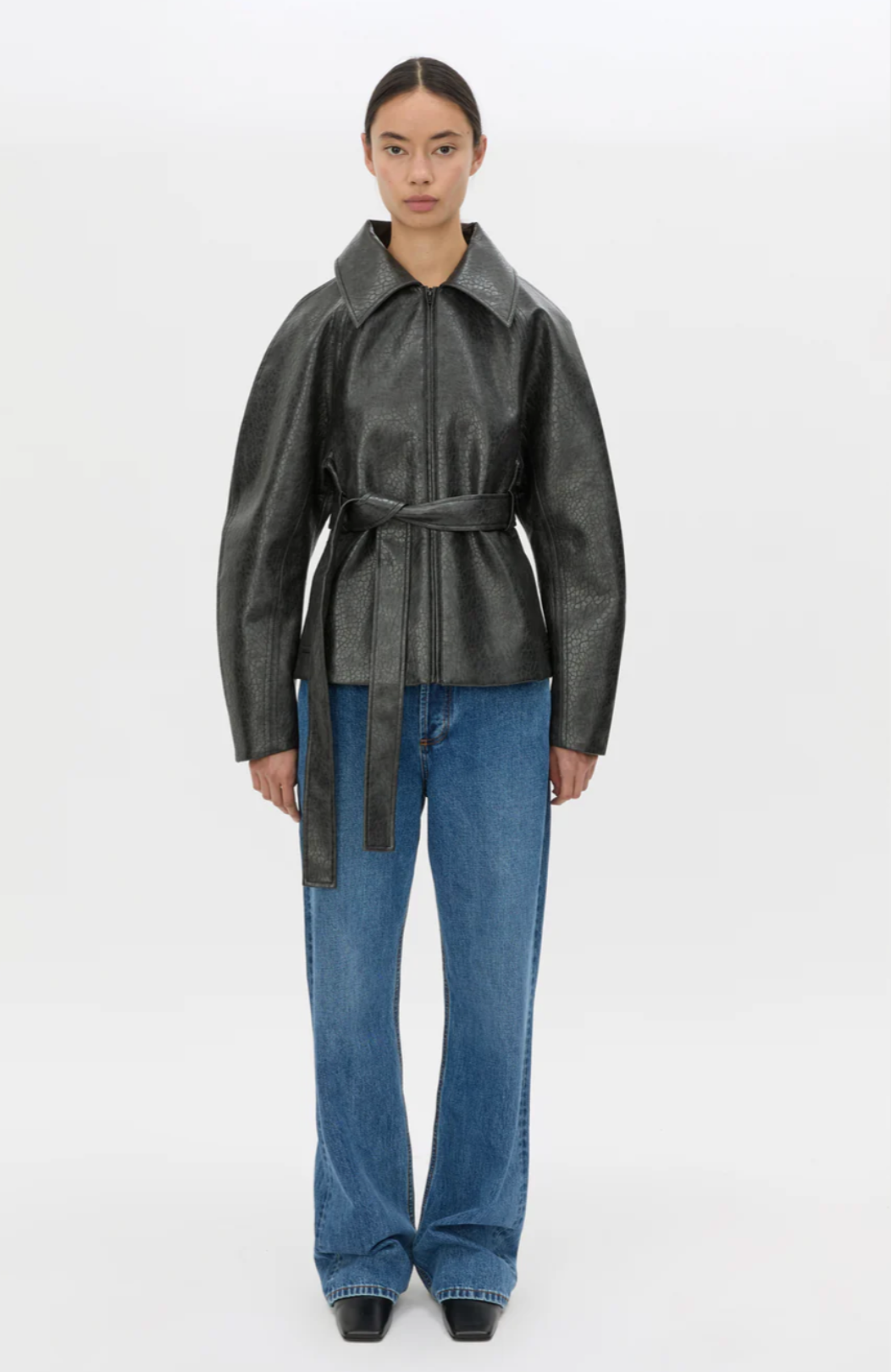 Person wearing a black leather jacket and blue jeans on a white background