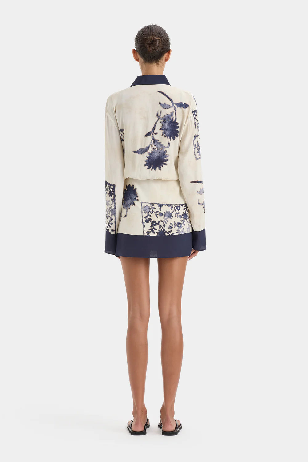 Person wearing a cream-colored blazer with blue floral patterns on a white background
