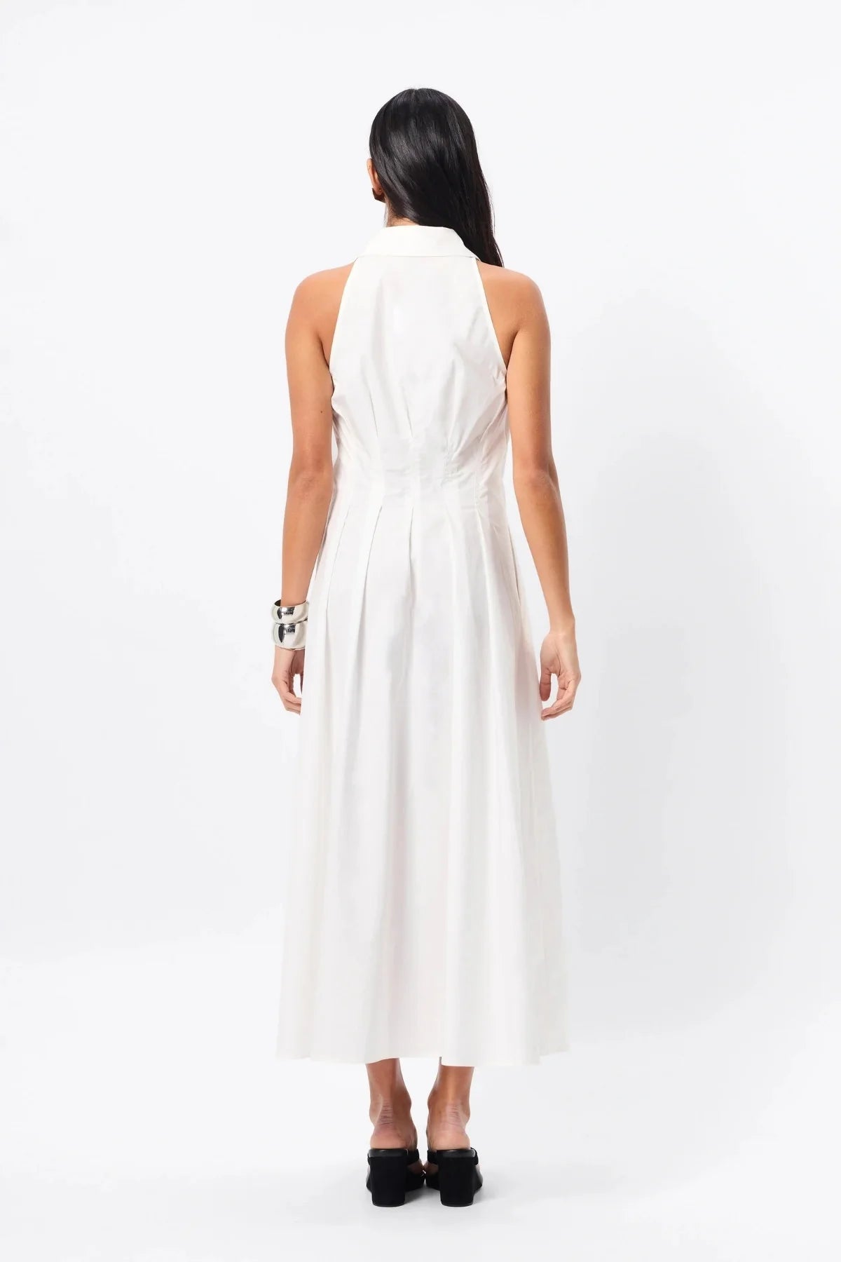 A woman standing in a white cotton day dress with pleat detail— a refined take on the classic shirt dress with timeless appeal.
Crafted from premium Australian cotton, this sleeveless midi features a structured collared neckline, racerback detail, and a fitted bodice that flows into a semi-flared A-line skirt. Stitch detailing at the fixed waist enhances the silhouette, while functional side pockets add everyday ease. Designed for the modern minimalist, this effortless style transitions seamlessly from day