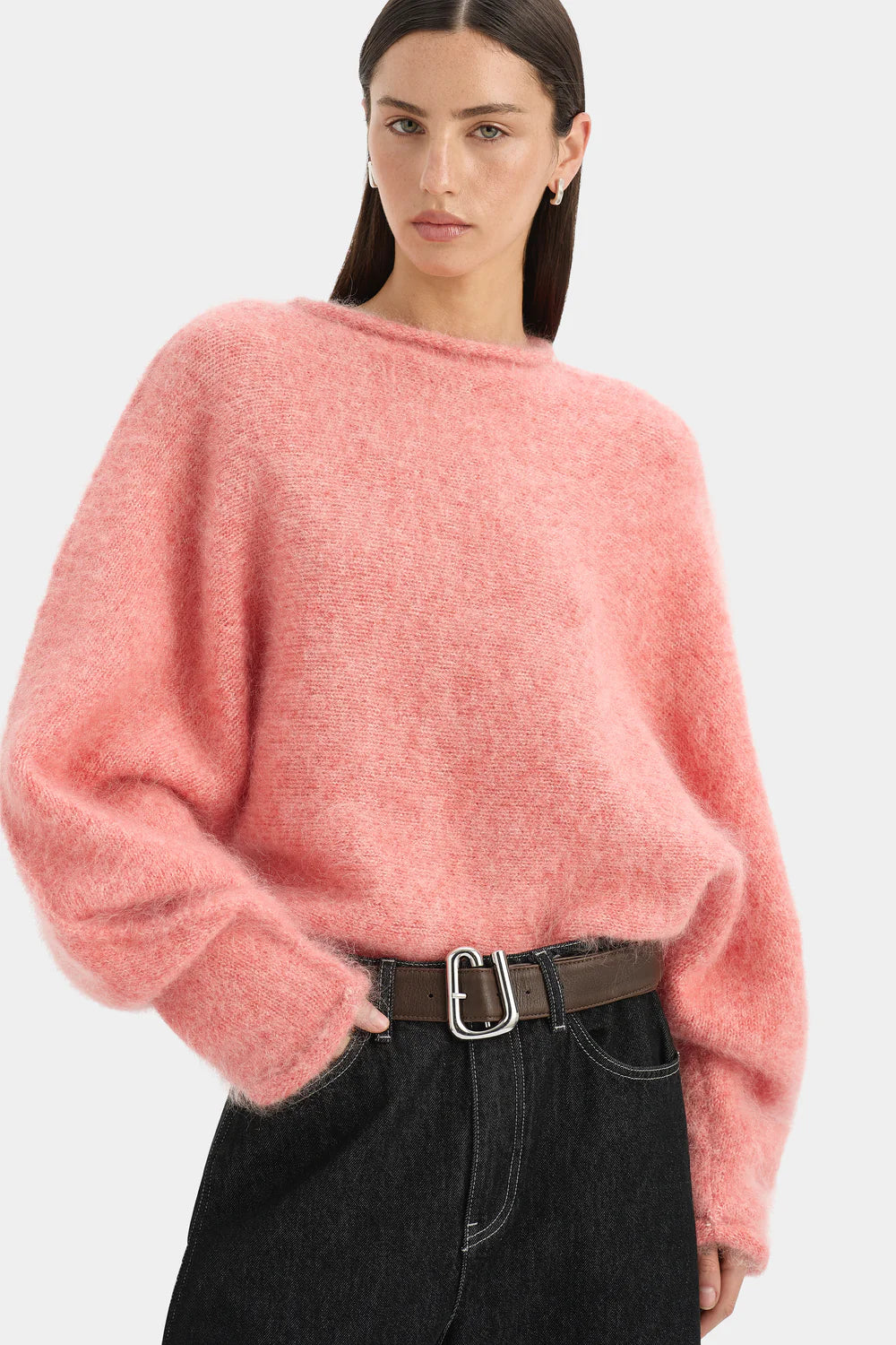 Person wearing a pink sweater and black pants on a white background