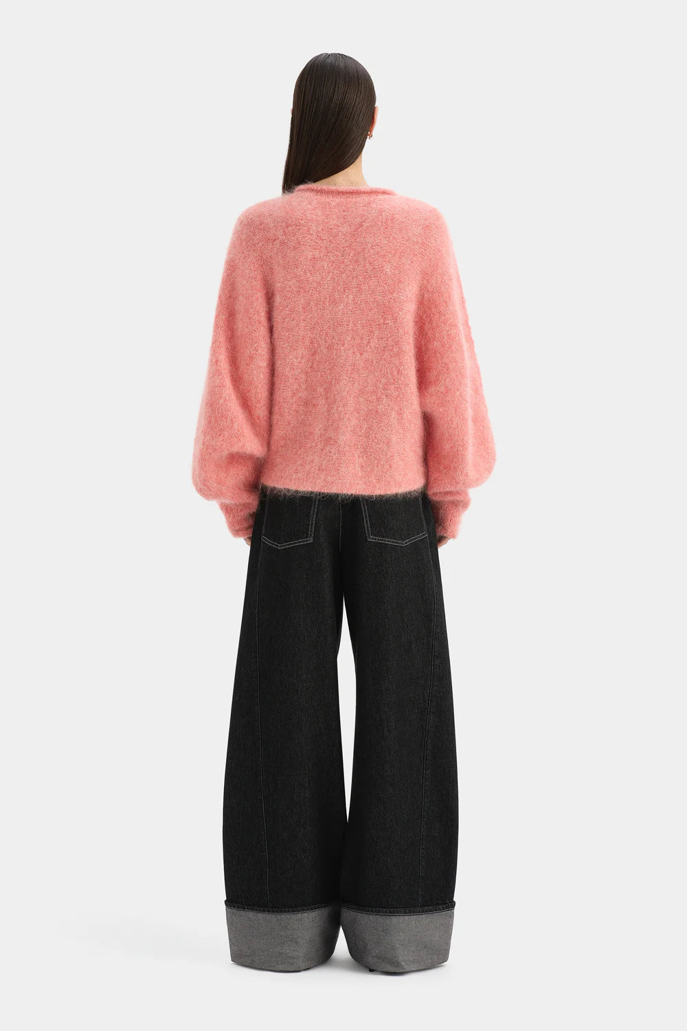 Person wearing a pink sweater and black wide-leg pants on a white background