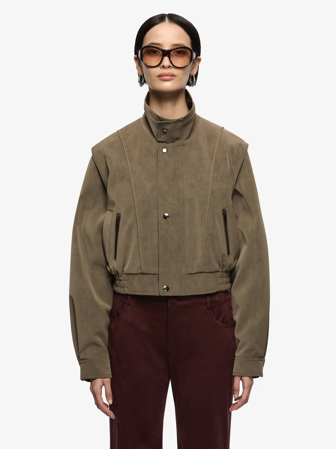Zoli Bomber in Olive. A chic faux-suede bomber perfect for layering. Designed with panel detailing, internal wadding for warmth, elasticated waistband, and metal press-stud closures, combining structure with relaxed comfort.