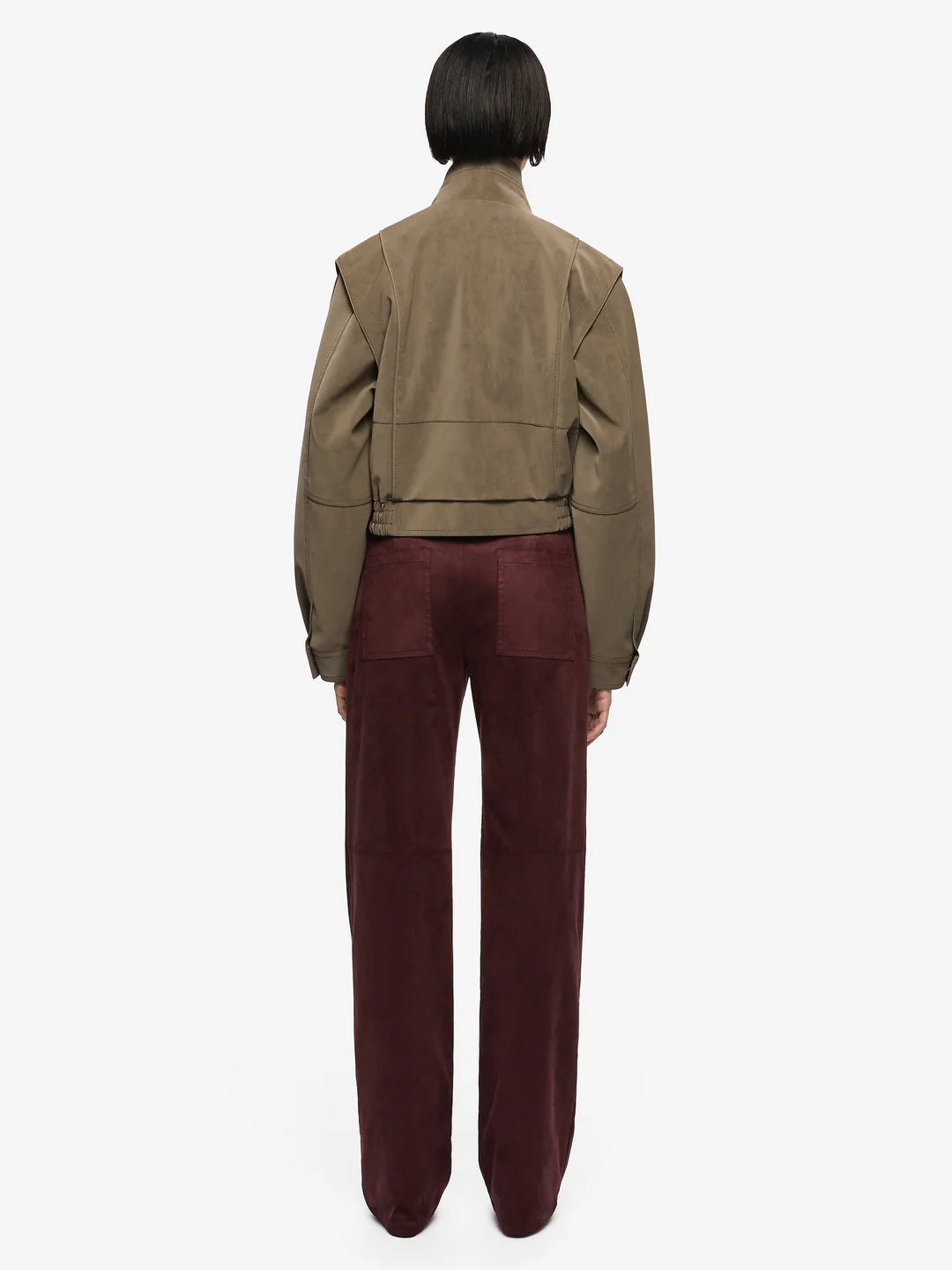 Zoli Bomber in Olive. A chic faux-suede bomber perfect for layering. Designed with panel detailing, internal wadding for warmth, elasticated waistband, and metal press-stud closures, combining structure with relaxed comfort.