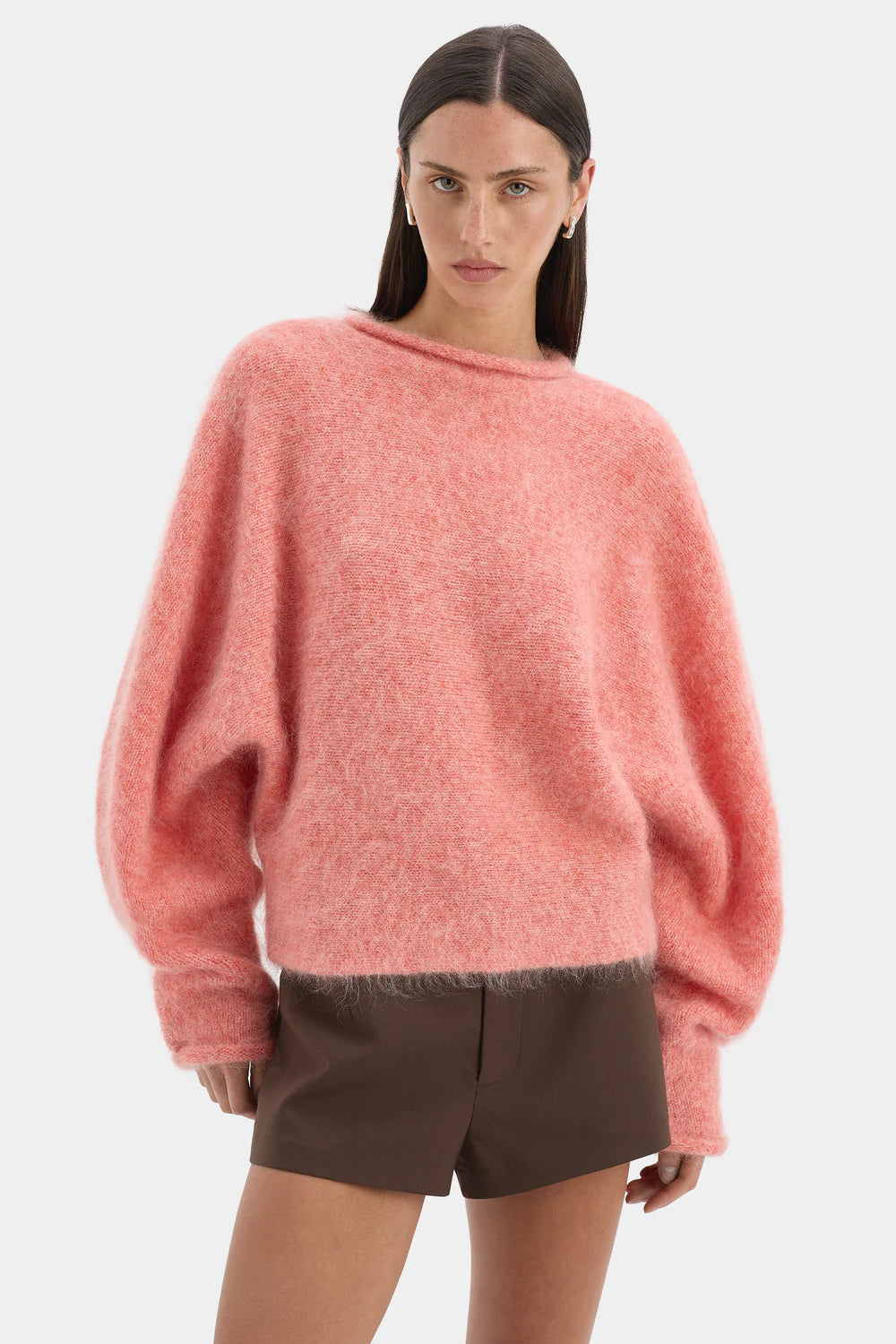 Woman wearing a pink sweater and brown shorts on a white background