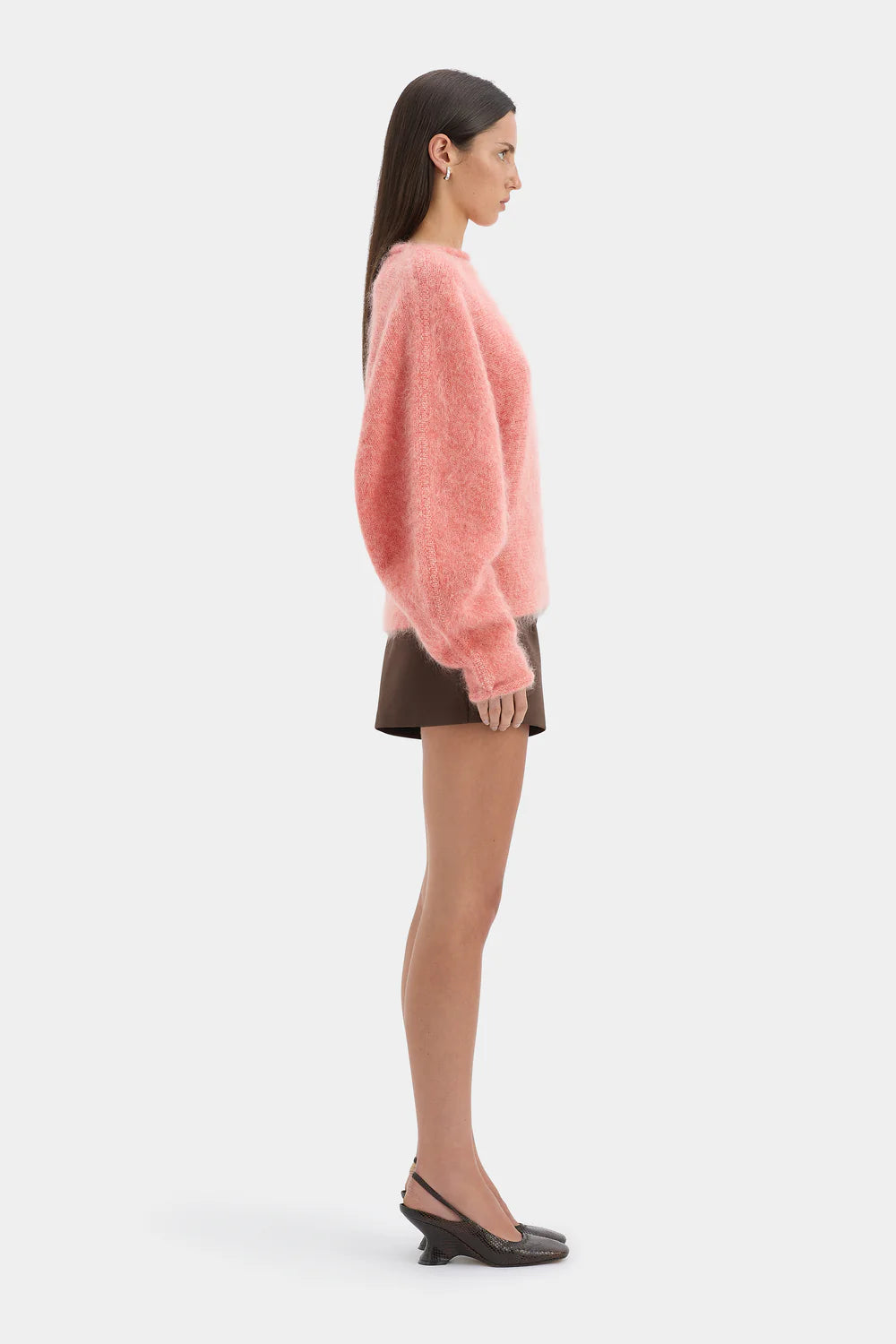 Woman wearing a pink sweater and brown skirt on a white background