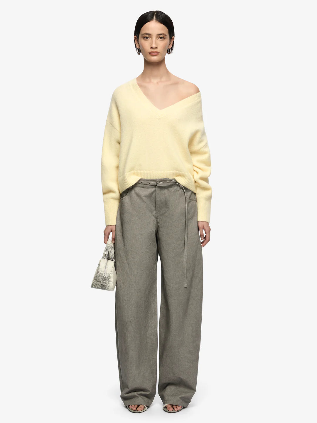 Woman wearing a yellow sweater and gray pants on a white background