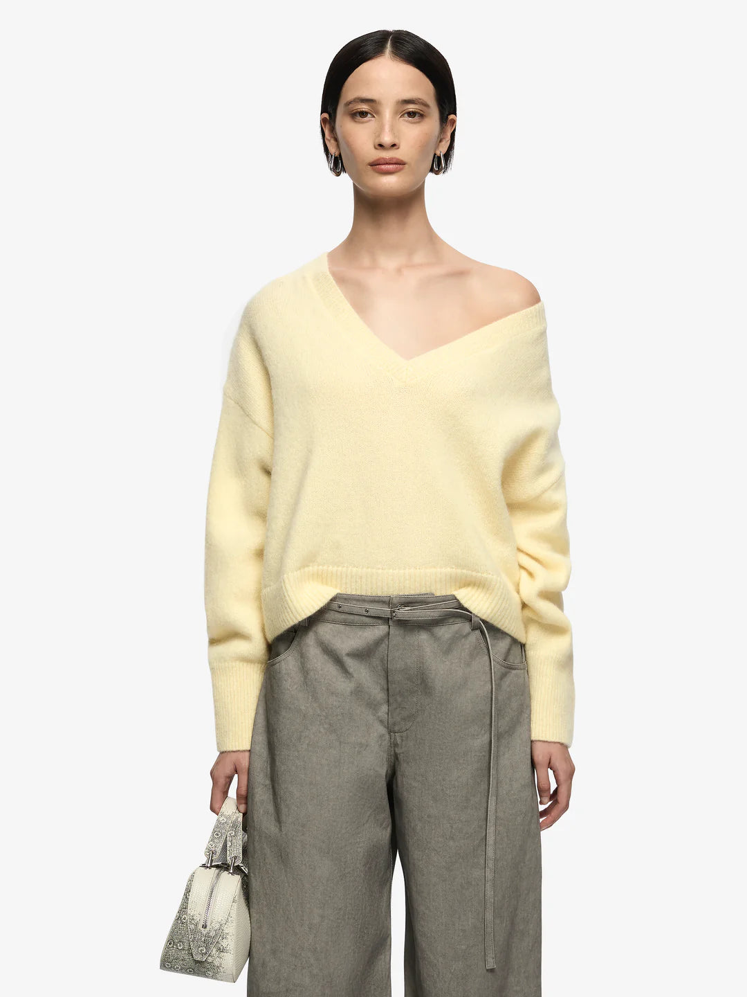 Woman wearing a light yellow sweater and gray pants on a white background