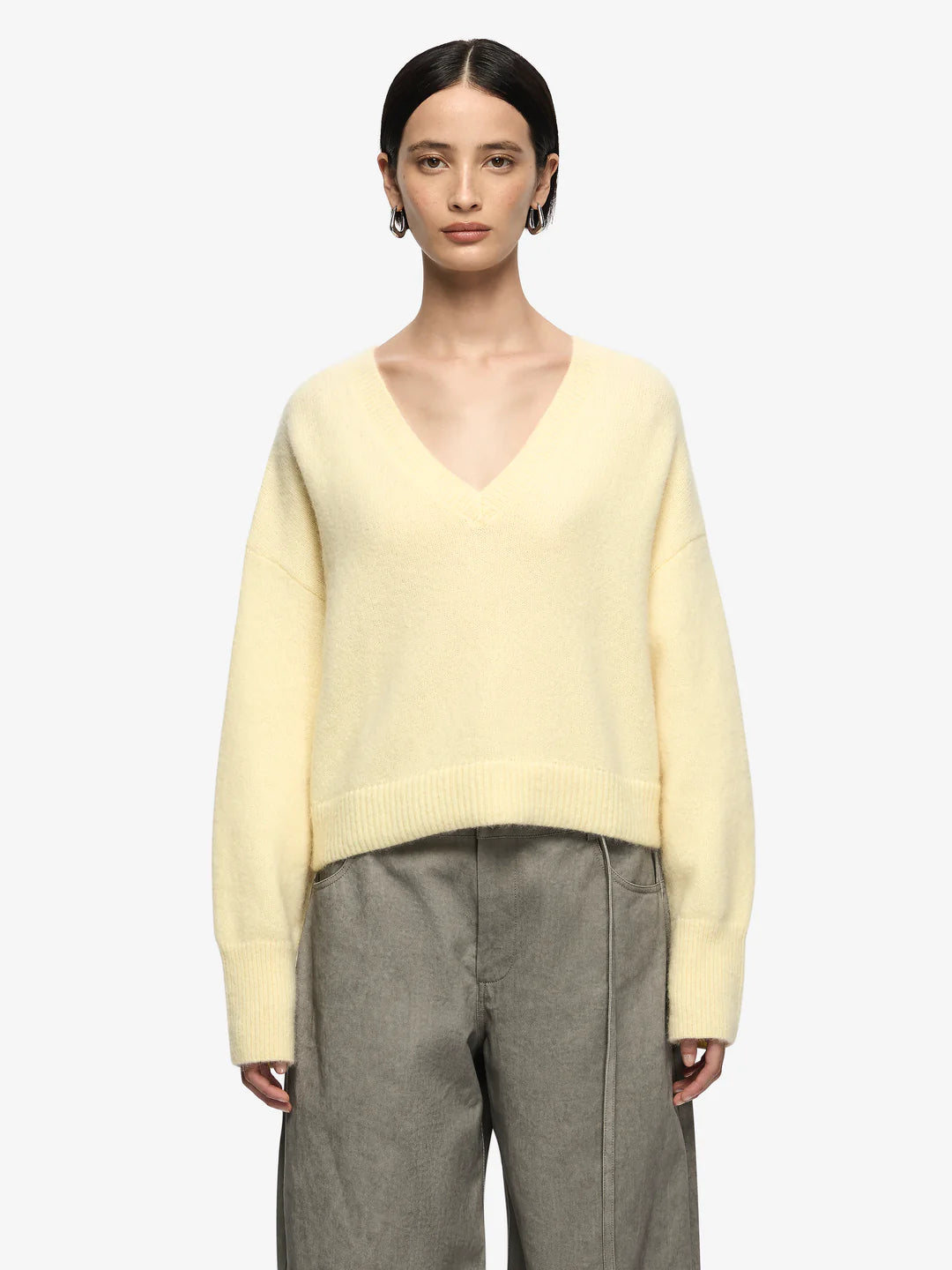 Person wearing a light yellow sweater and gray pants on a white background
