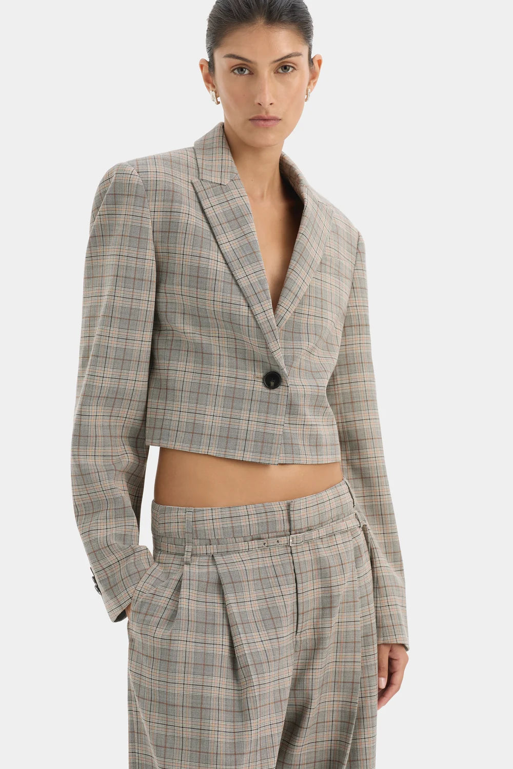 A model wearing a cropped, single-breasted plaid blazer and matching high-waisted trousers in a beige and gray check pattern, set against a plain light gray background.