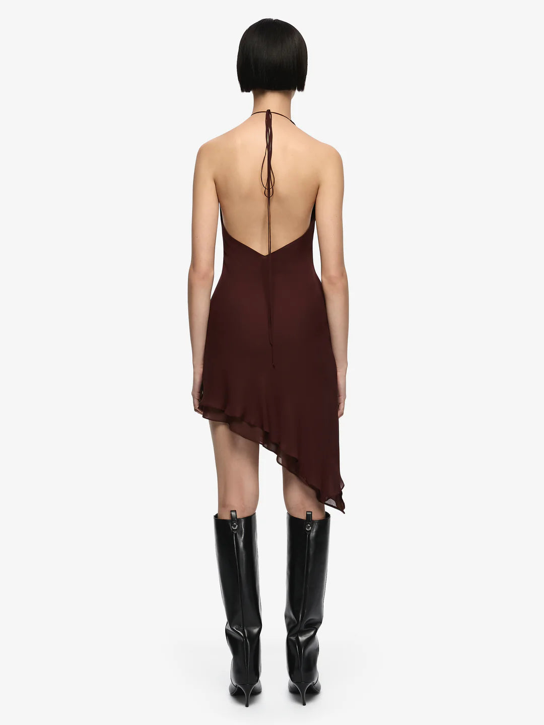 Woman wearing a brown dress with a backless design and black knee-high boots on a white background