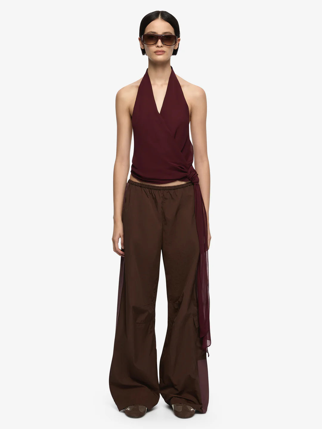 Woman wearing a burgundy halter top and brown wide-leg pants on a white background