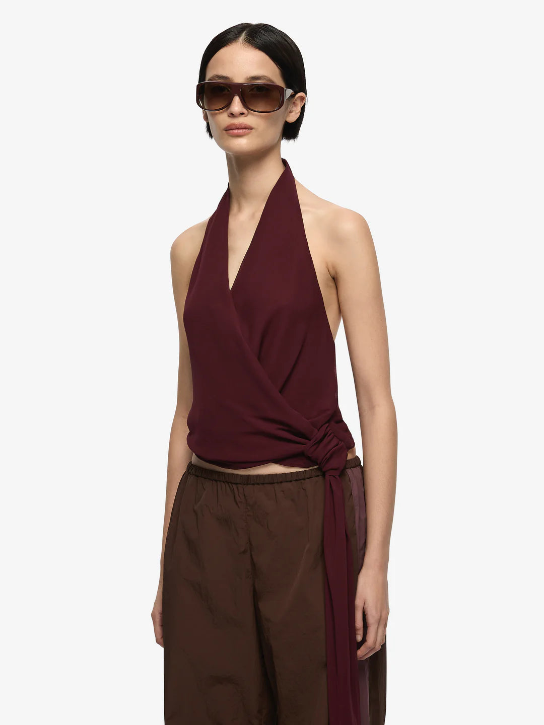 Woman wearing a burgundy halter top and brown pants on a white background