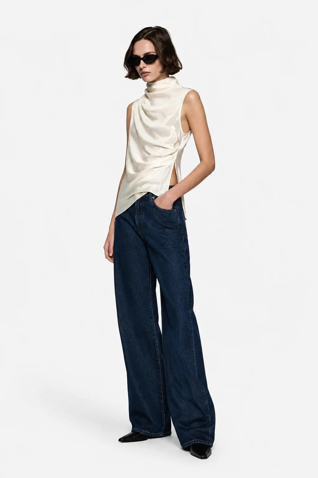 Woman wearing a white sleeveless top and blue wide-leg pants on a white background