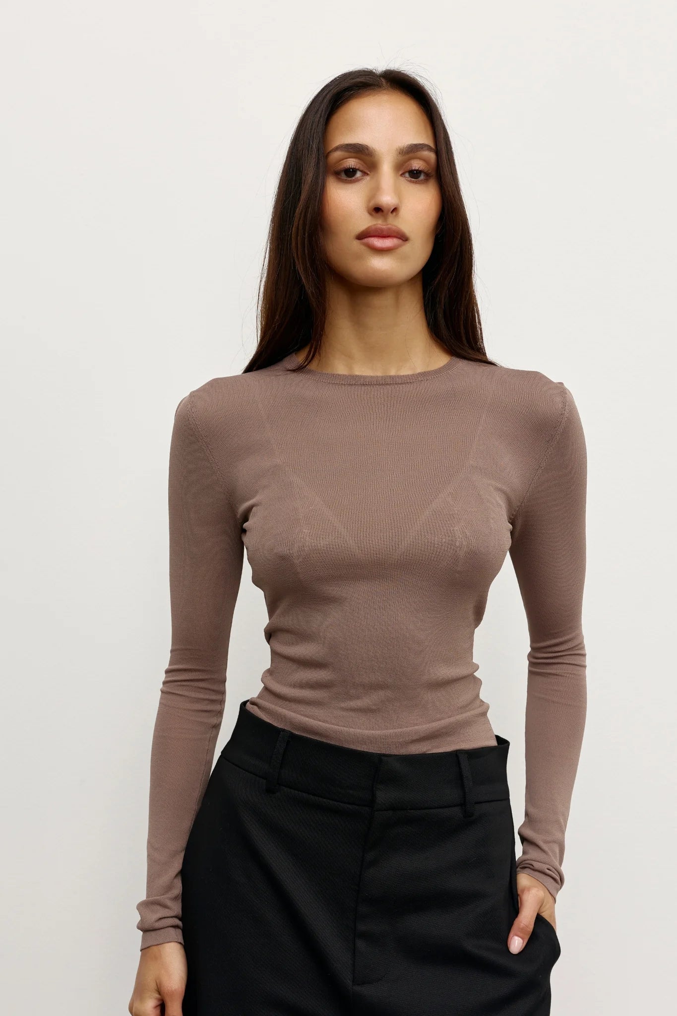 A woman in a brown fitted top with black pants on white background