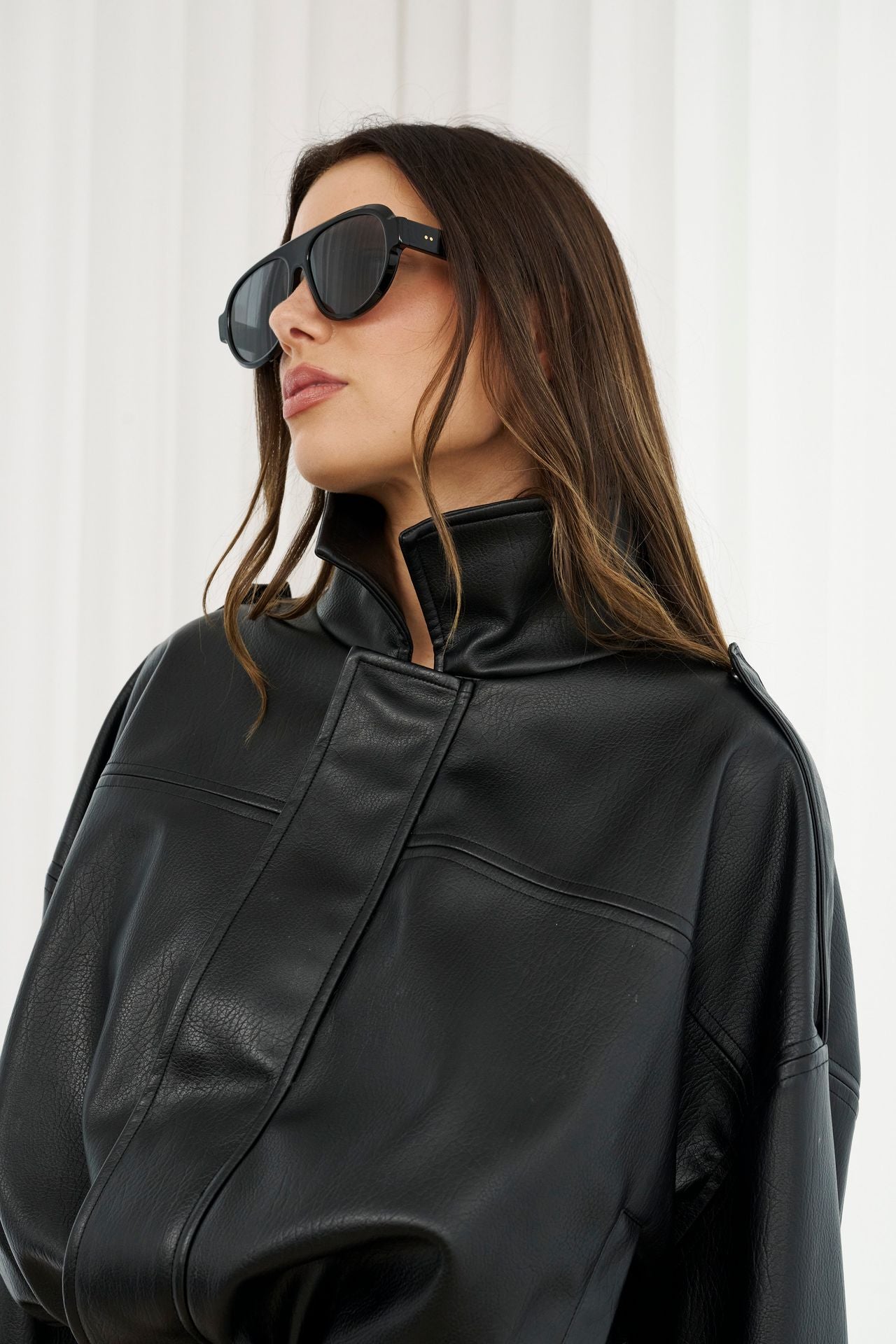 Woman wearing a black leather jacket and sunglasses against a white background