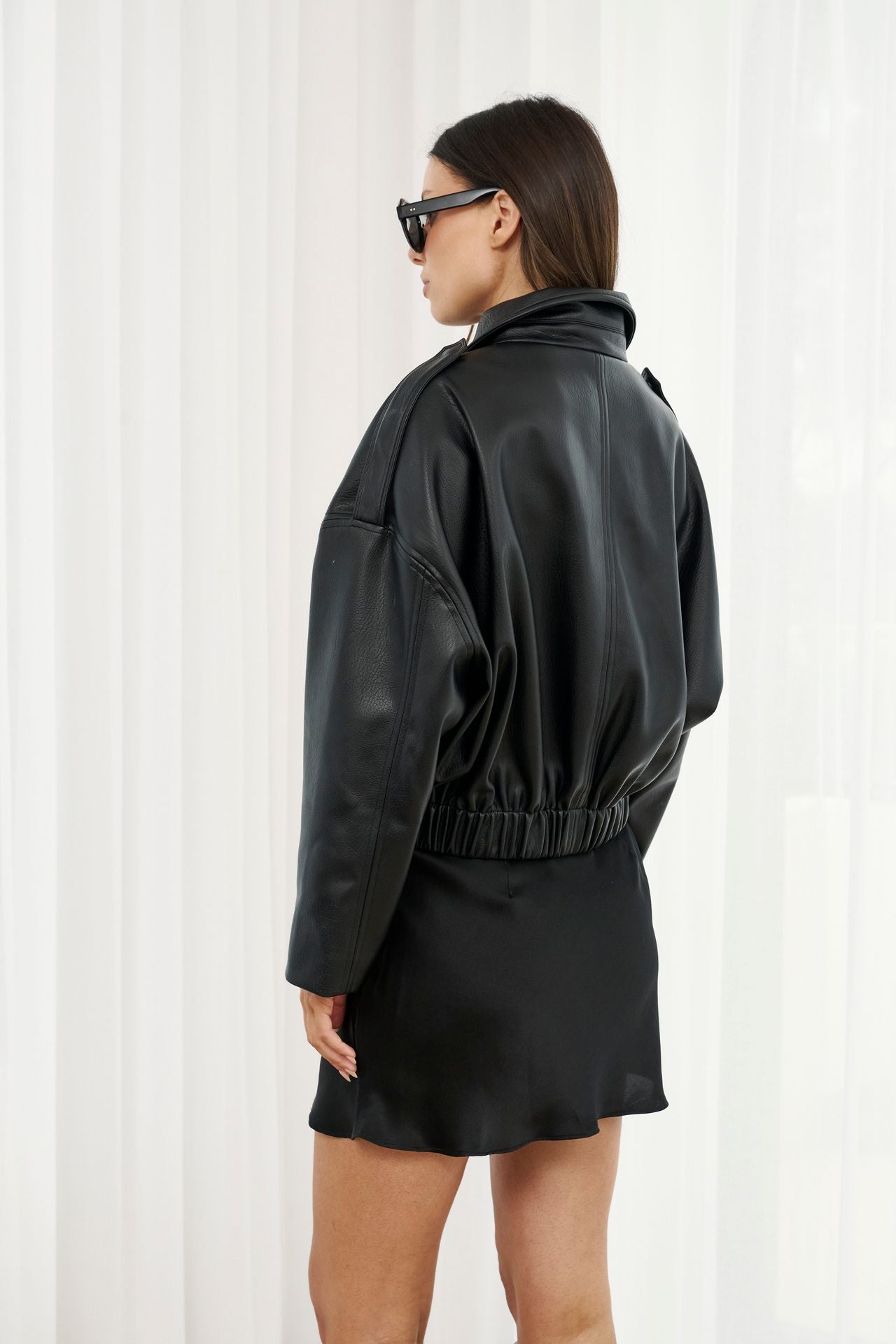 Woman wearing a black leather jacket and dress against a white background