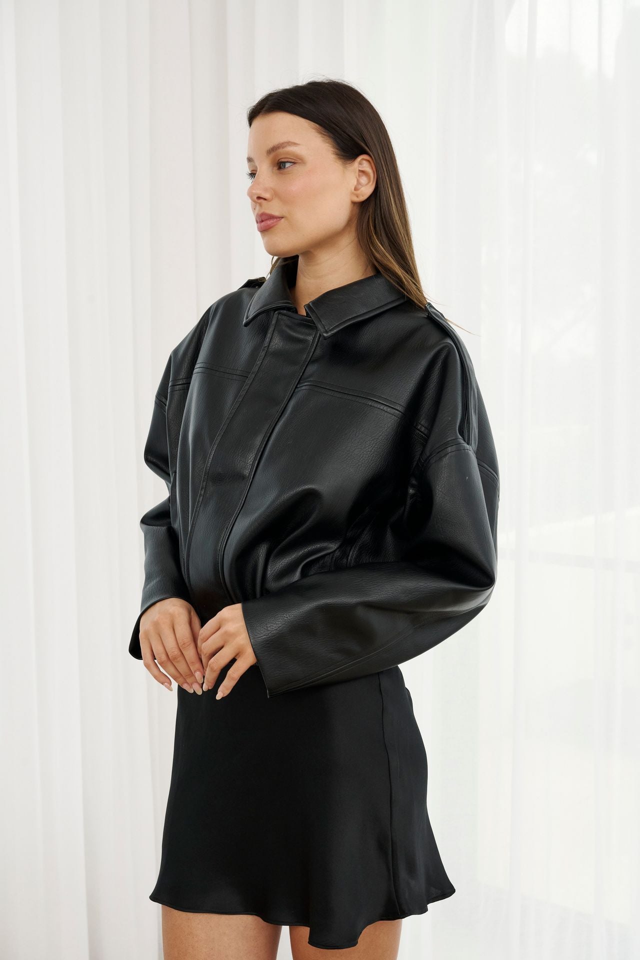 Woman wearing a black leather jacket against a white curtain background
