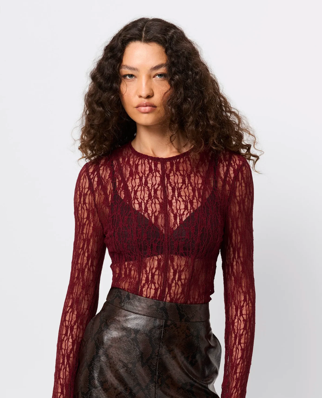 Woman wearing a burgundy lace top with black leather pants on a white background