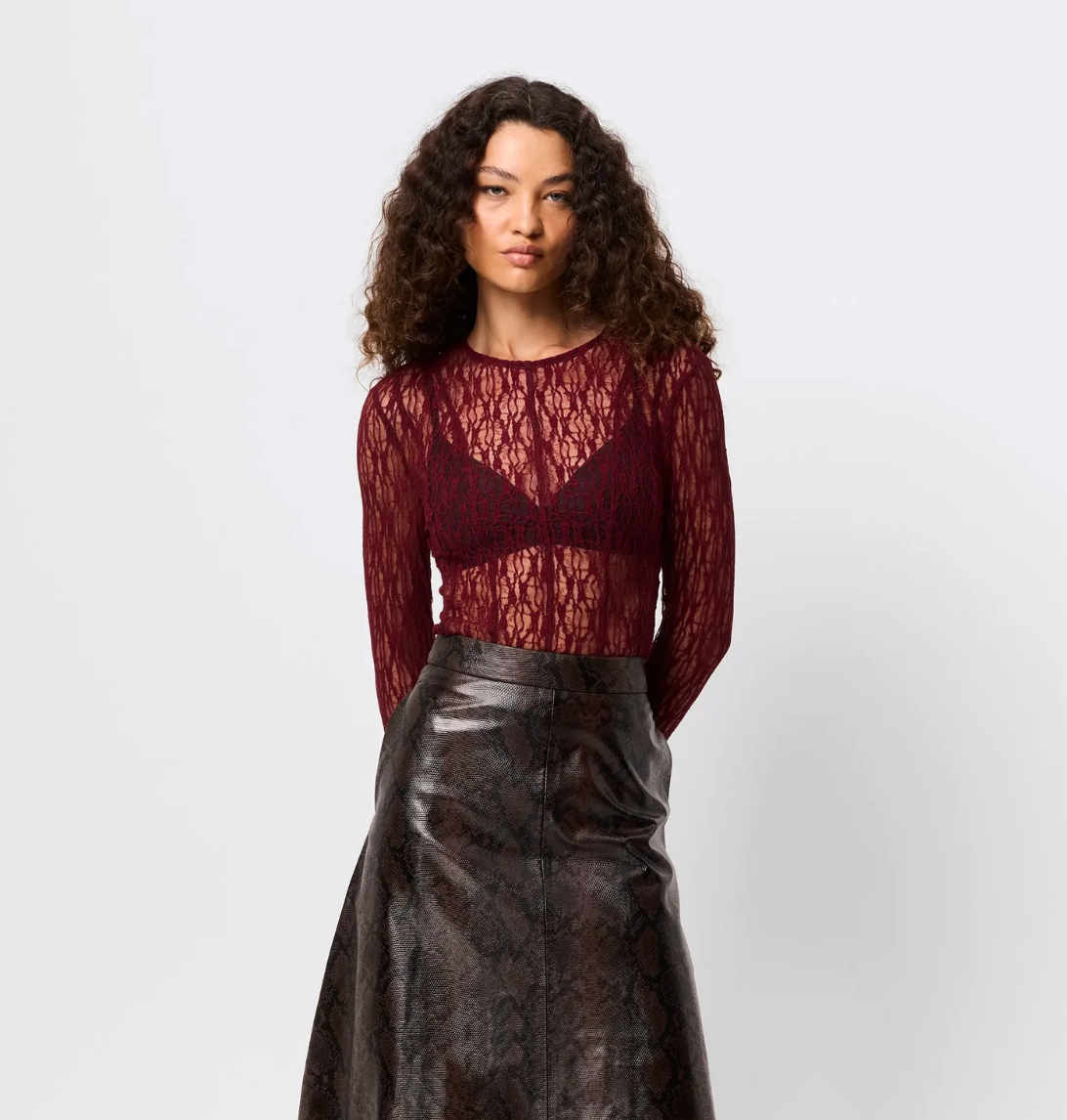 Woman wearing a burgundy lace top and black leather skirt on a white background